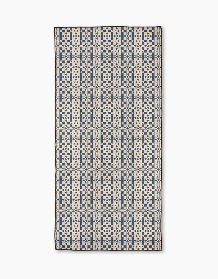 The Geometry Intermission Blue Micro-loop Beach Towel features a grid-like geometric pattern of navy squares and lines on cream, made from quick-drying, post-consumer recycled materials.
