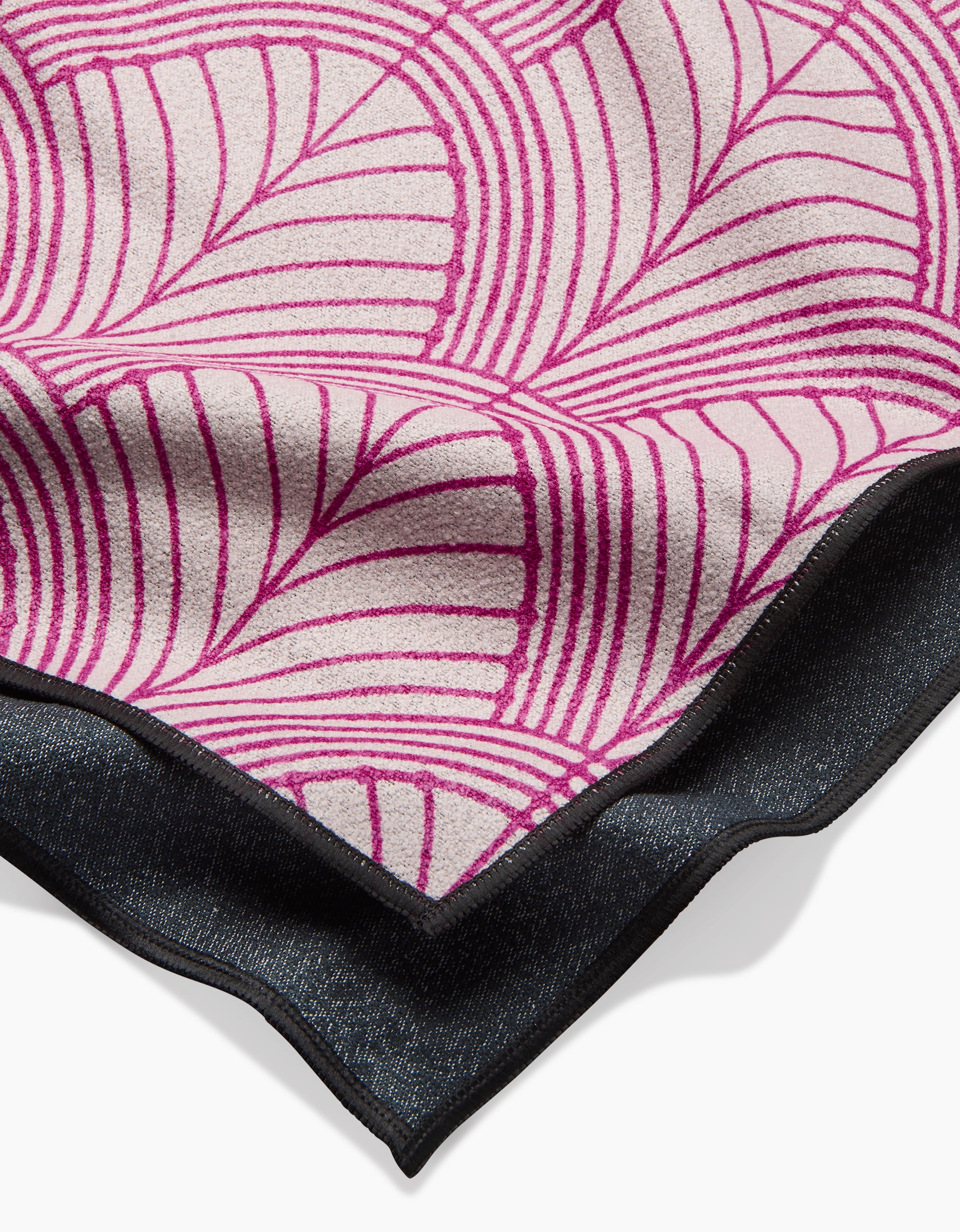 A close-up of the folded Jaskin beach towel by Amy MacCready, showing its bold pink and cream geometric leaf pattern on quick-drying recycled material, with a dark textured edge beneath the design.
