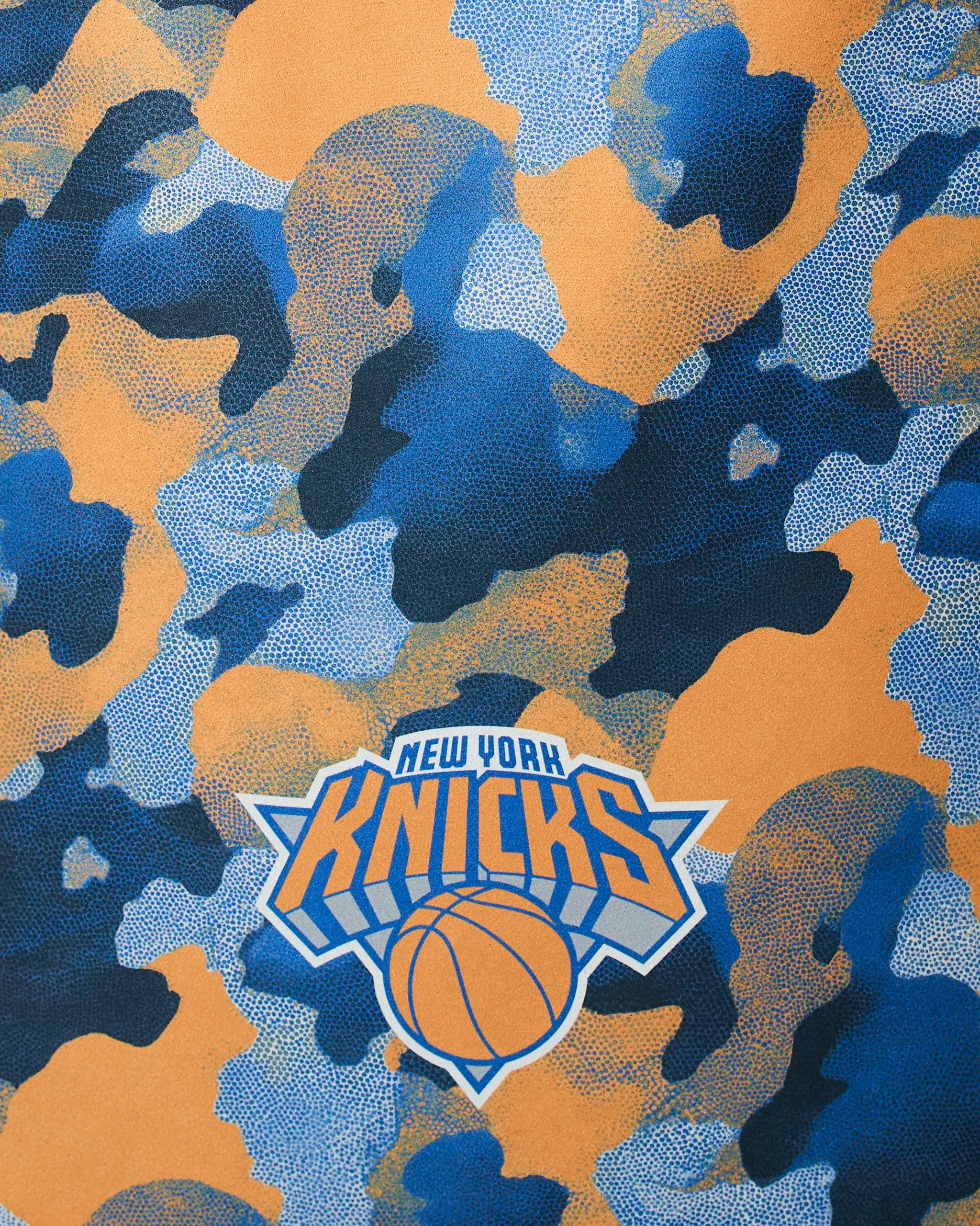 The Geometry Knicks Camo showcases a blue and orange camouflage pattern with the New York Knicks logo, basketball, and starburst design at the center.