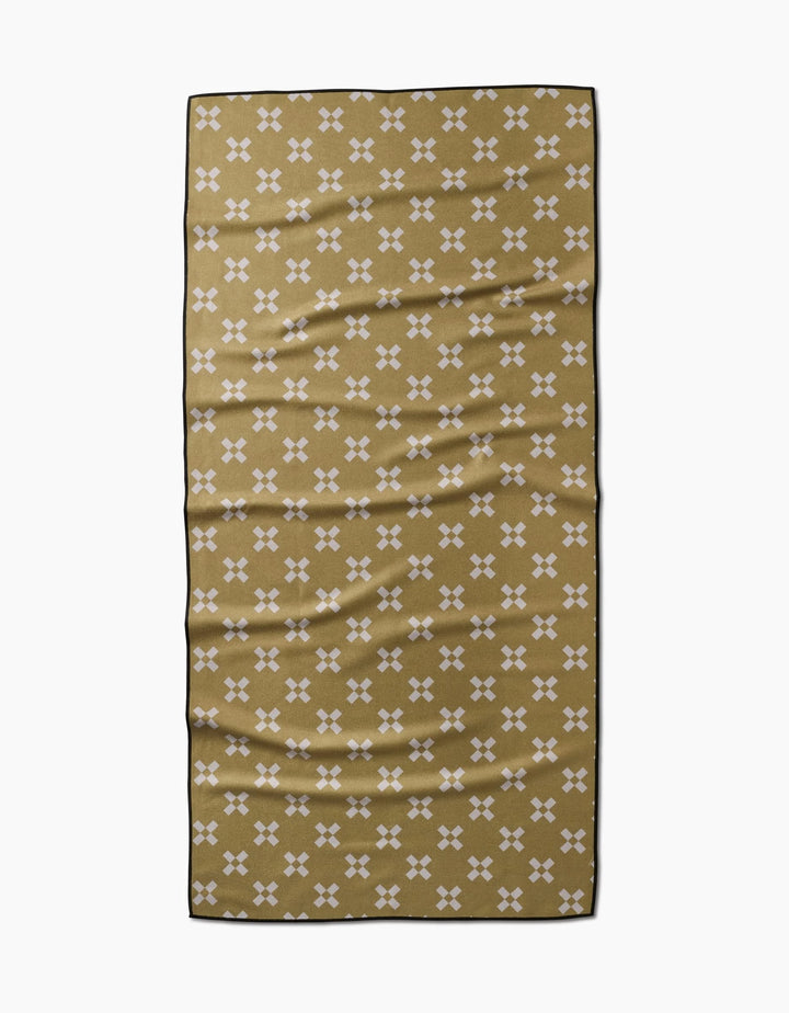 The Lina towel by Anna Christian is a rectangular olive green quick-drying piece with small white X patterns and a thin black border, shown laid flat with gentle folds on a white background.