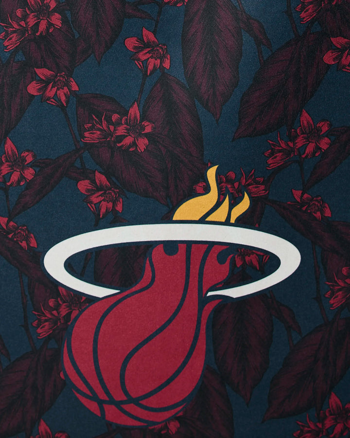 The image features the Miami Heat logo—a flaming basketball with a white hoop—set against a dark blue background with red flowers, inspiring the Heat Floral NBA beach towel by NBALAB x Geometry, made from recycled materials.