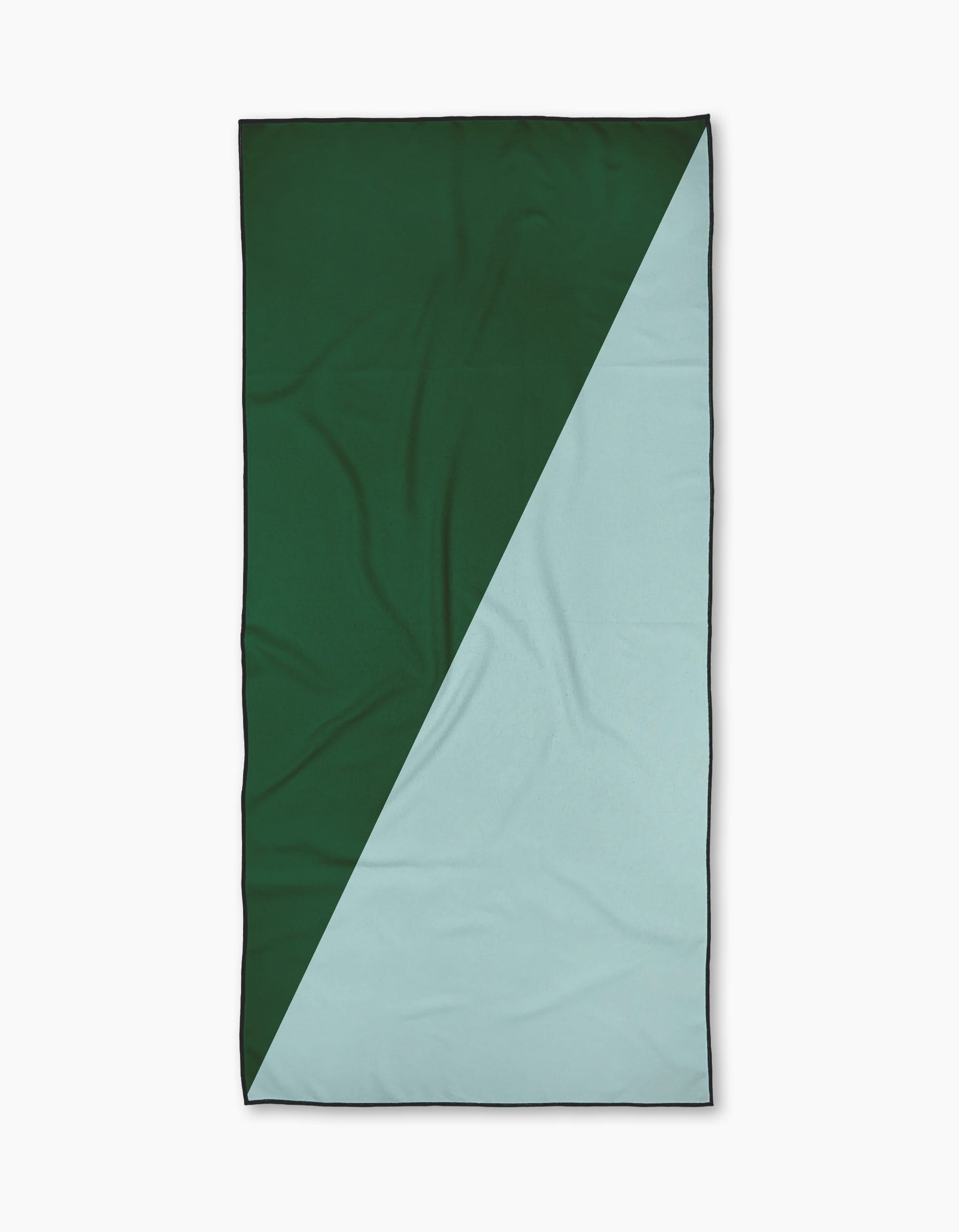 The Minted Oasis beach towel by Geometry is rectangular with a diagonal color split—dark green upper left, light blue lower right. Made from recycled materials, quick-drying, and shown flat with subtle wrinkles.