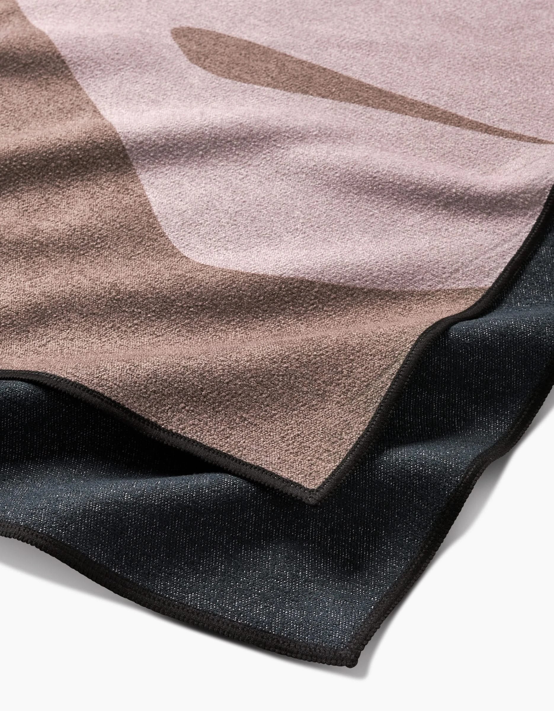A close-up of PrintedPlants Monstera Leaf towel, featuring abstract shapes in brown, mauve, and black on soft, quick-drying recycled fabric with a textured feel and neatly finished edges.