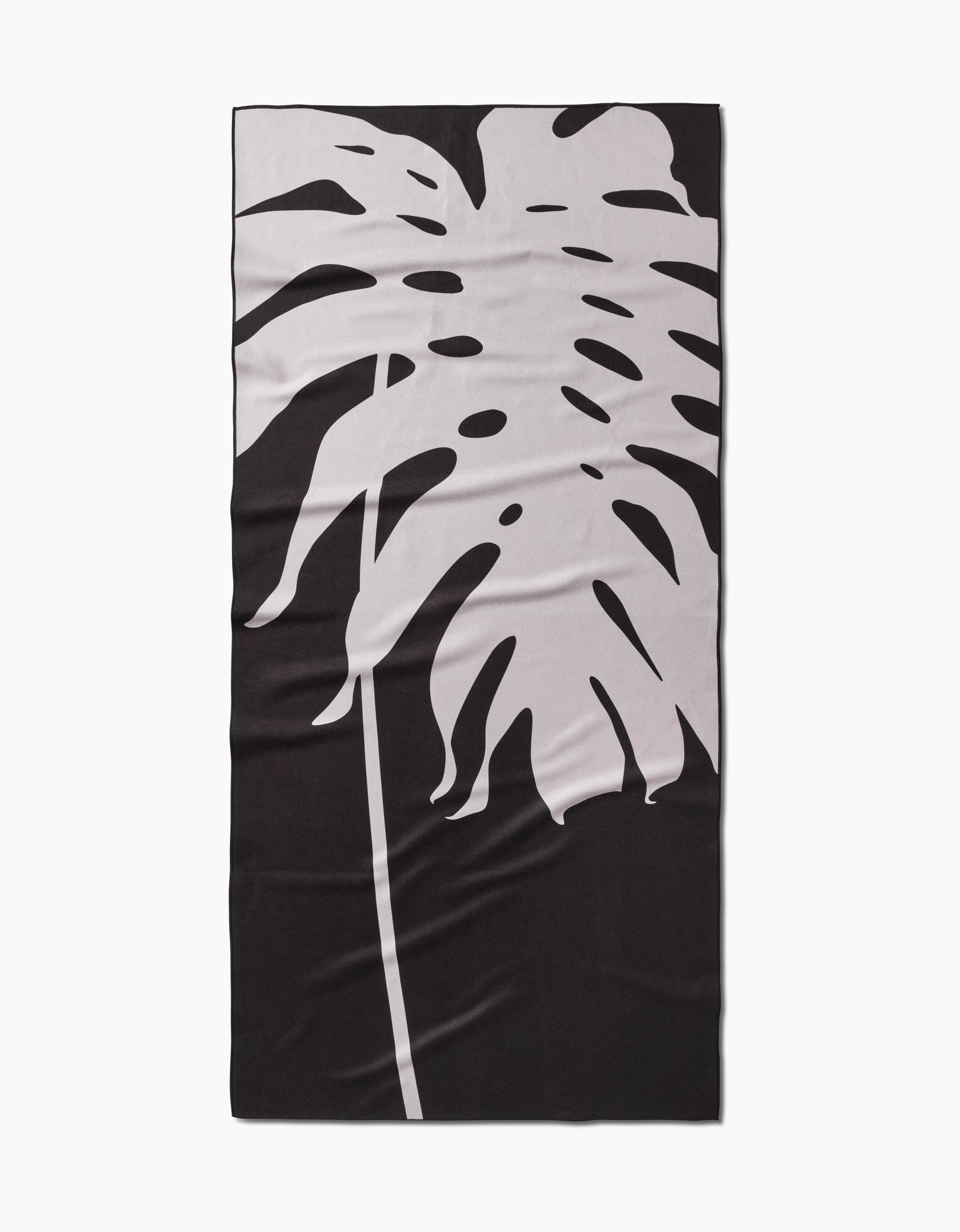The PrintedPlant Monstera Beach Towel is a rectangular black microfiber towel featuring a bold, diagonal light monstera leaf print and crafted with quick-drying fabric for easy style and convenience.