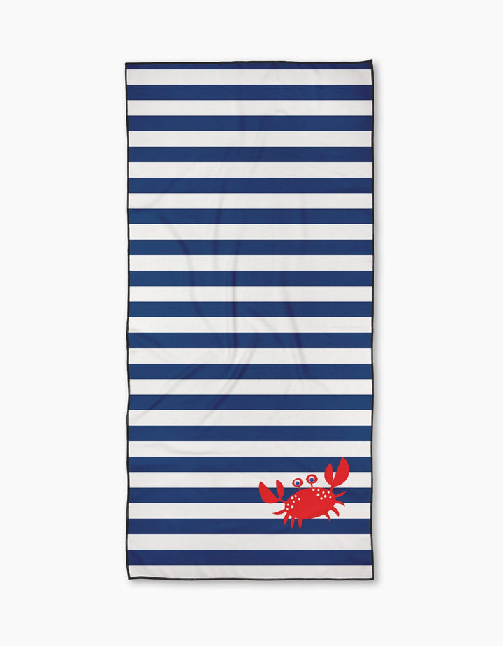 The Geometry Nautical Nipper is a rectangular beach towel made from quick-drying recycled materials, showcasing navy and white horizontal stripes with a small red cartoon crab in the bottom right corner.