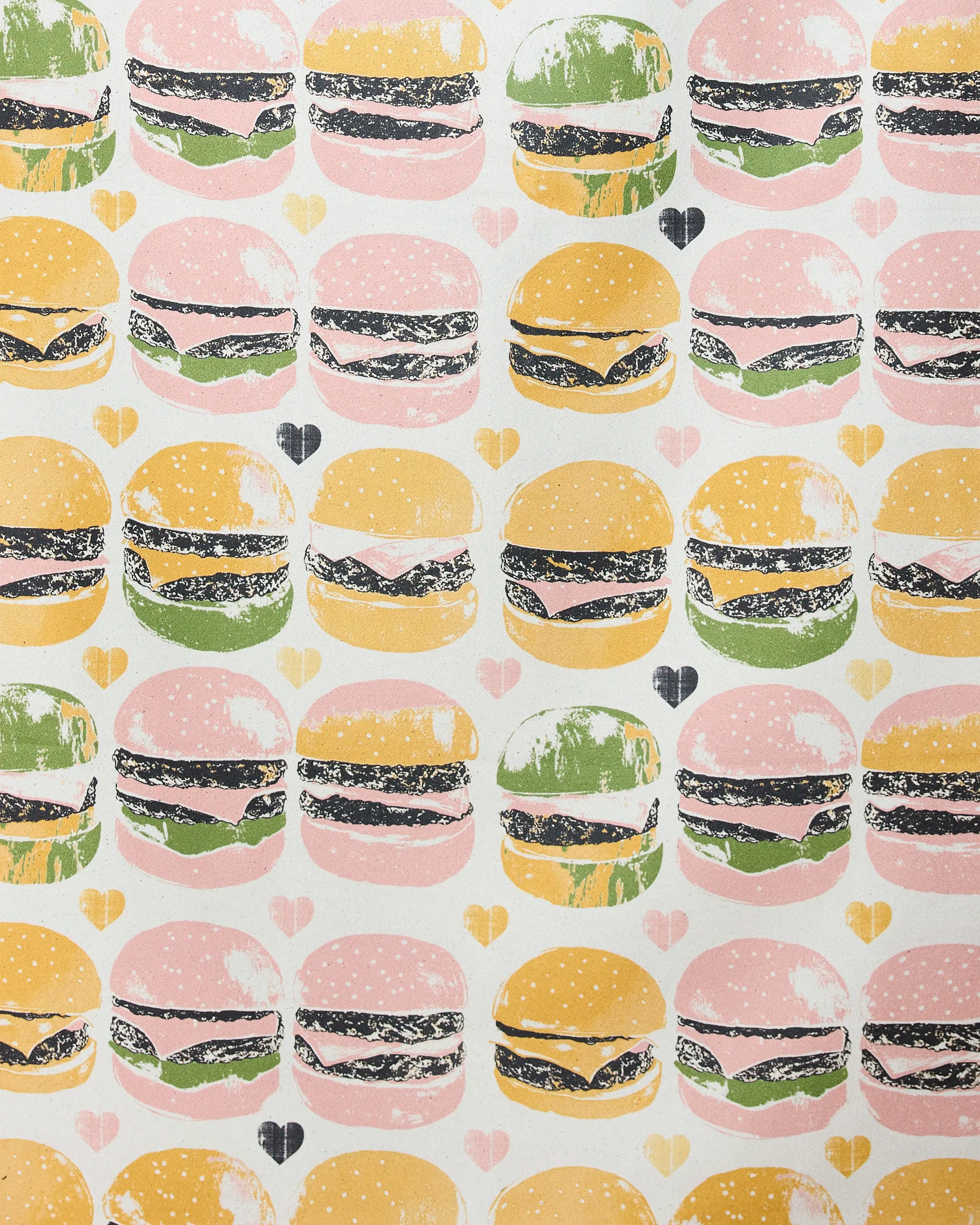 Geometry’s “On The Grill” beach towel features a quick-drying white background with a playful illustrated hamburger pattern in pink, yellow, and green, accented by small hearts.