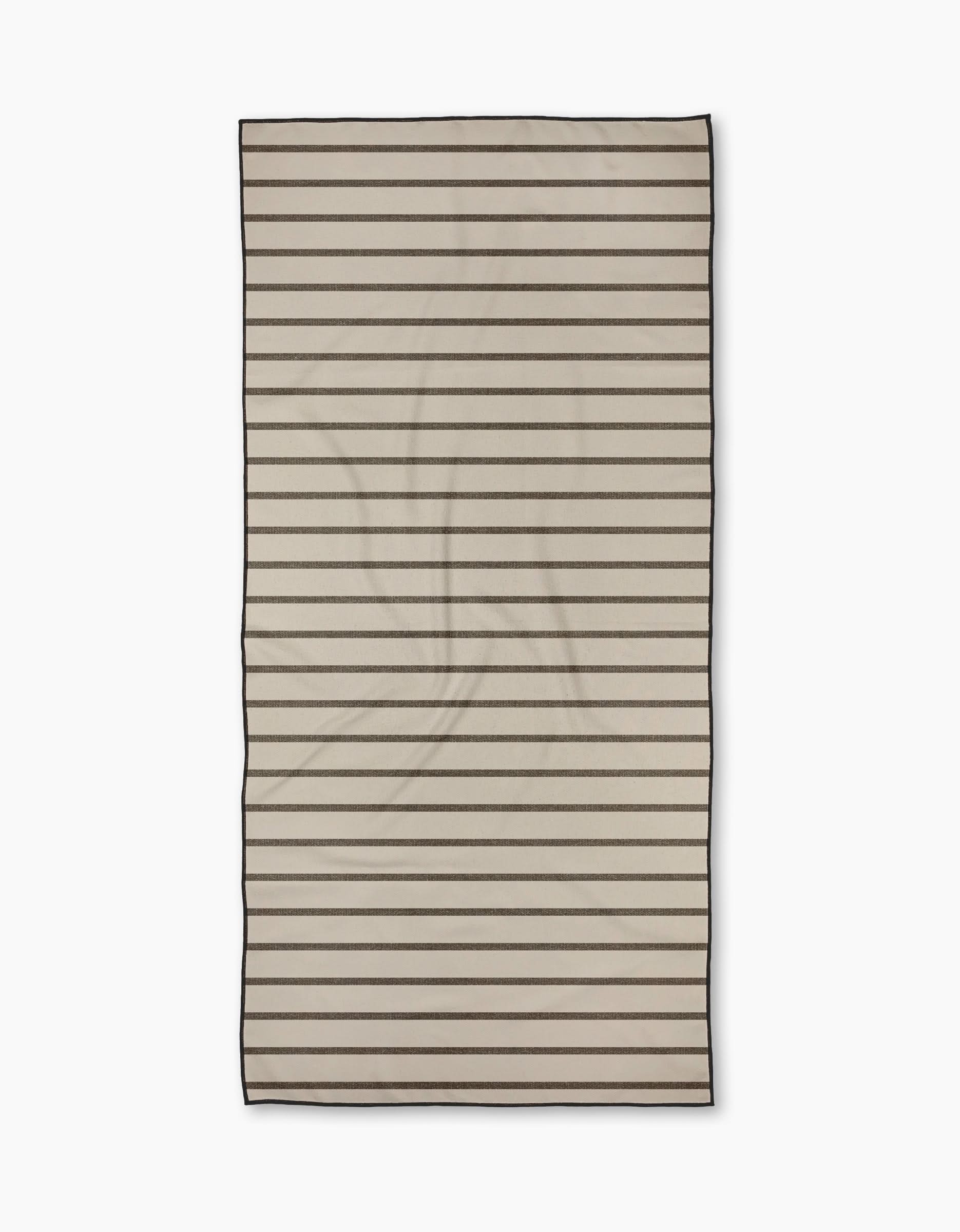 The Jenny Keller Salt Air Stripe beach towel is beige, rectangular, and quick-drying with evenly spaced thin black horizontal stripes and black edging, shown flat on a white background.