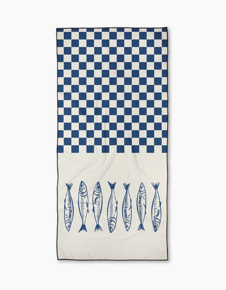 The Sardine Check Blue towel by Hufton Studio features a blue and white checkerboard design on top and seven blue fish illustrations on a quick-drying, plain white lower half.