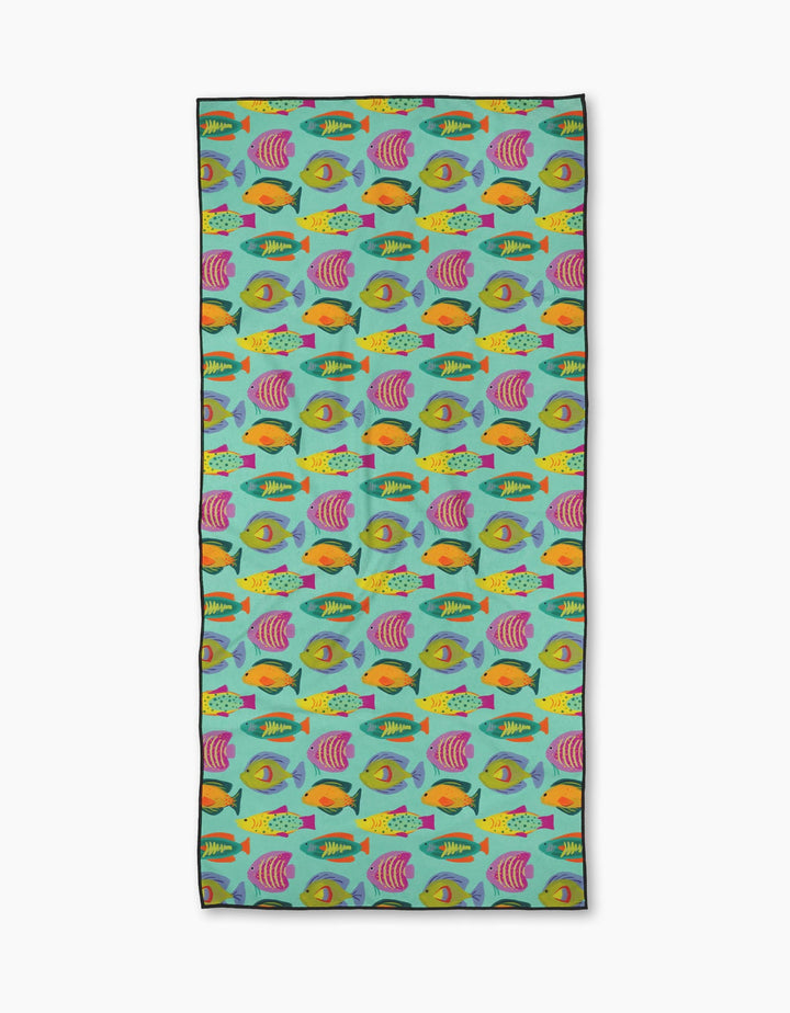 The Schooling Micro-loop Beach Towel by Geometry features a vibrant, repeating tropical fish pattern in orange, yellow, pink, green, and purple on turquoise. Made with recycled materials, this quick-drying towel is eco-friendly and stylish.
