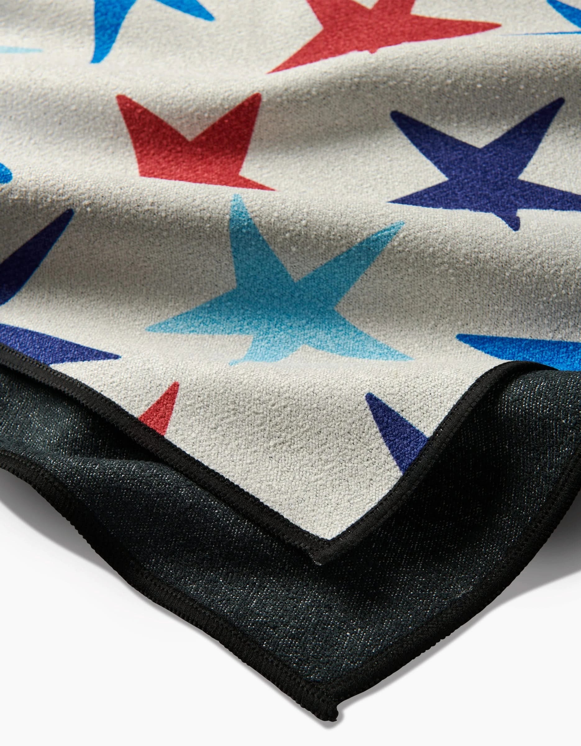 The Mindfulnice Seeing Stars blanket, made from post-consumer recycled materials, features a soft, light pattern of red and blue stars on pale fabric, layered over black with a textured edge and folded corner.