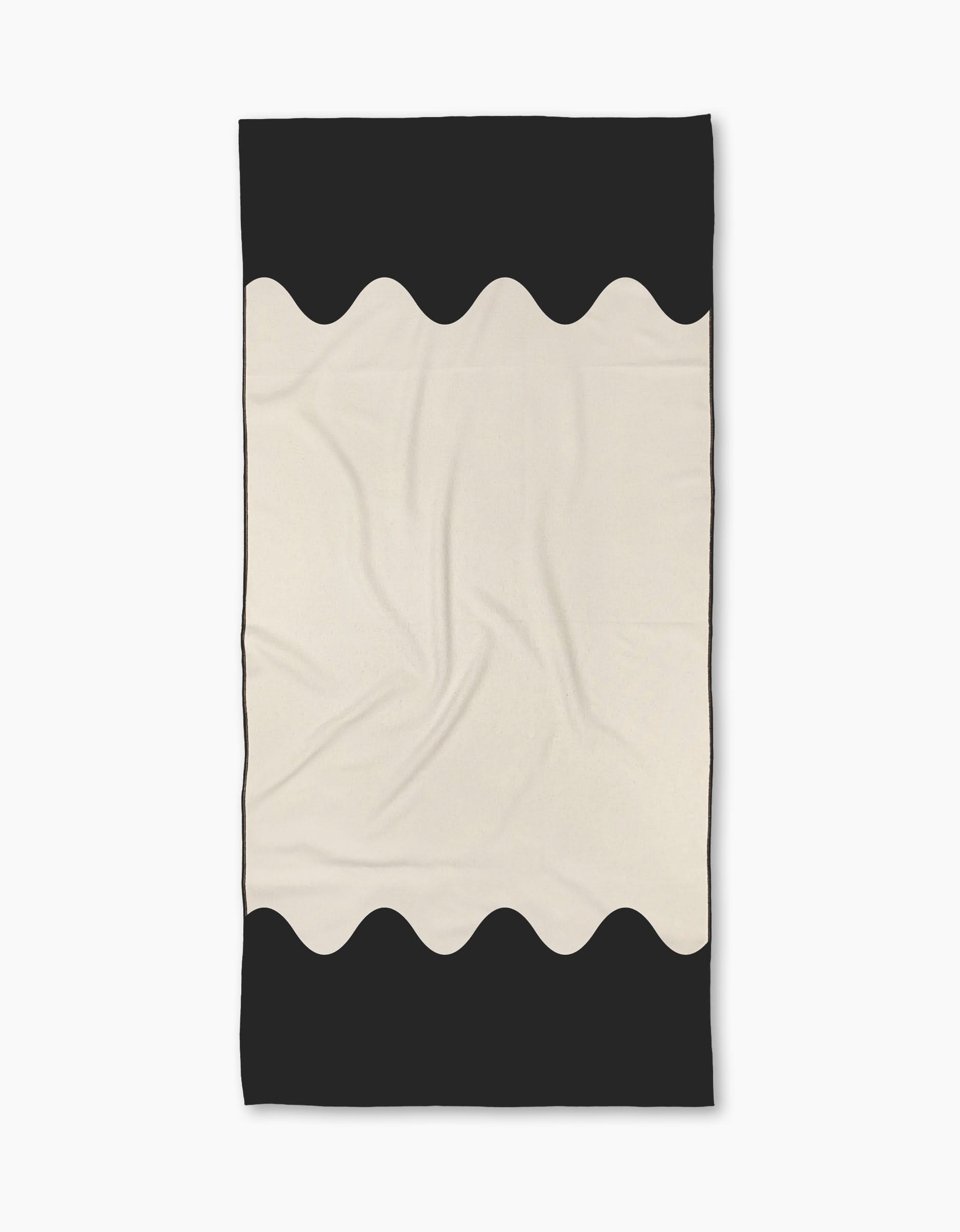 The Geometry Tide Line Micro-loop Beach Towel features a minimalist design with a cream center and wavy black borders. Made from recycled materials, the towel is shown flat with subtle folds and creases.