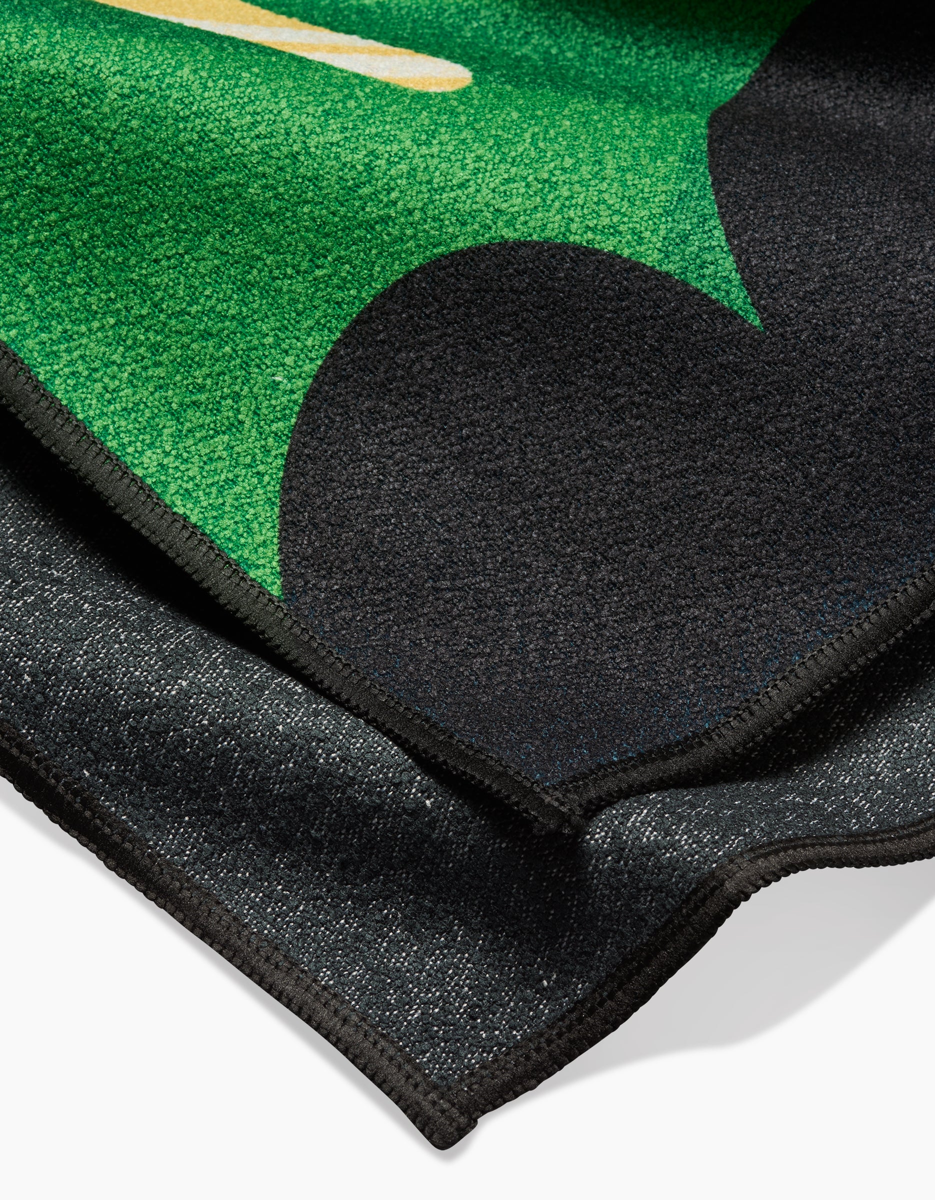 A close-up of Camila Leãos Water blanket shows a folded, textured fabric with green, black, and yellow abstract design and dark backing, crafted from recycled materials for an eco-friendly touch.
