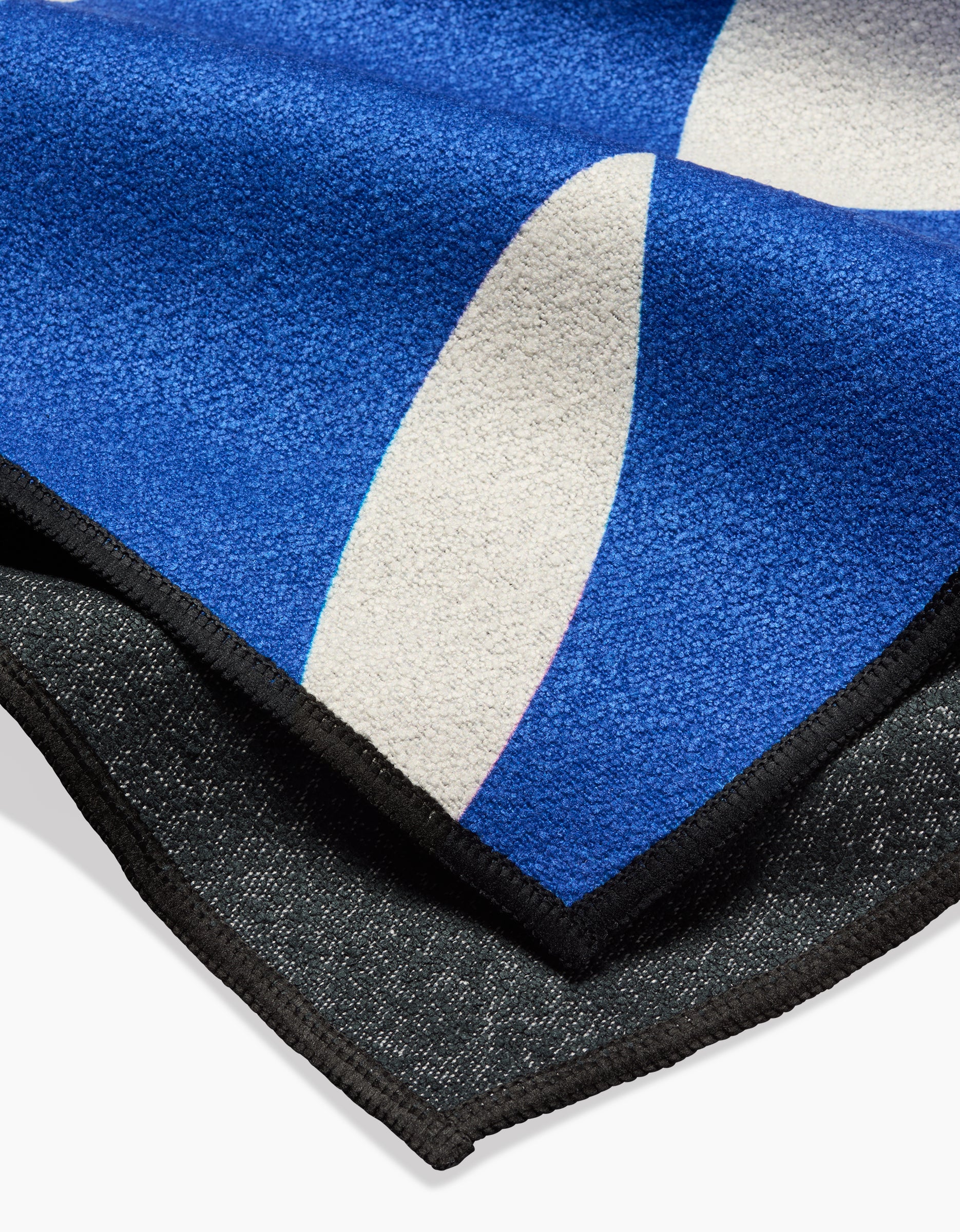 A close-up of two overlapping blankets: Claire Iglesias Wonky Lines blue quick-drying throw with white abstract shapes on top, layered over a subtly textured dark gray blanket.
