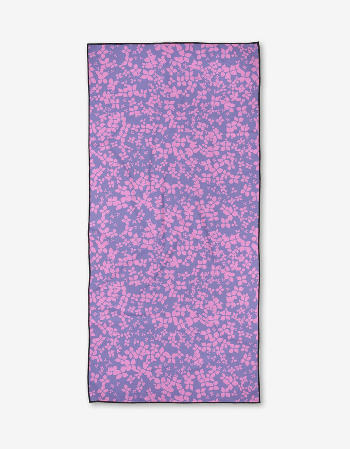 The Sareka Unique You Give Me Butterflies towel is a rectangular, quick-drying beach towel with a purple background and abstract pink shapes like pebbles or confetti, all outlined by a thin black border.