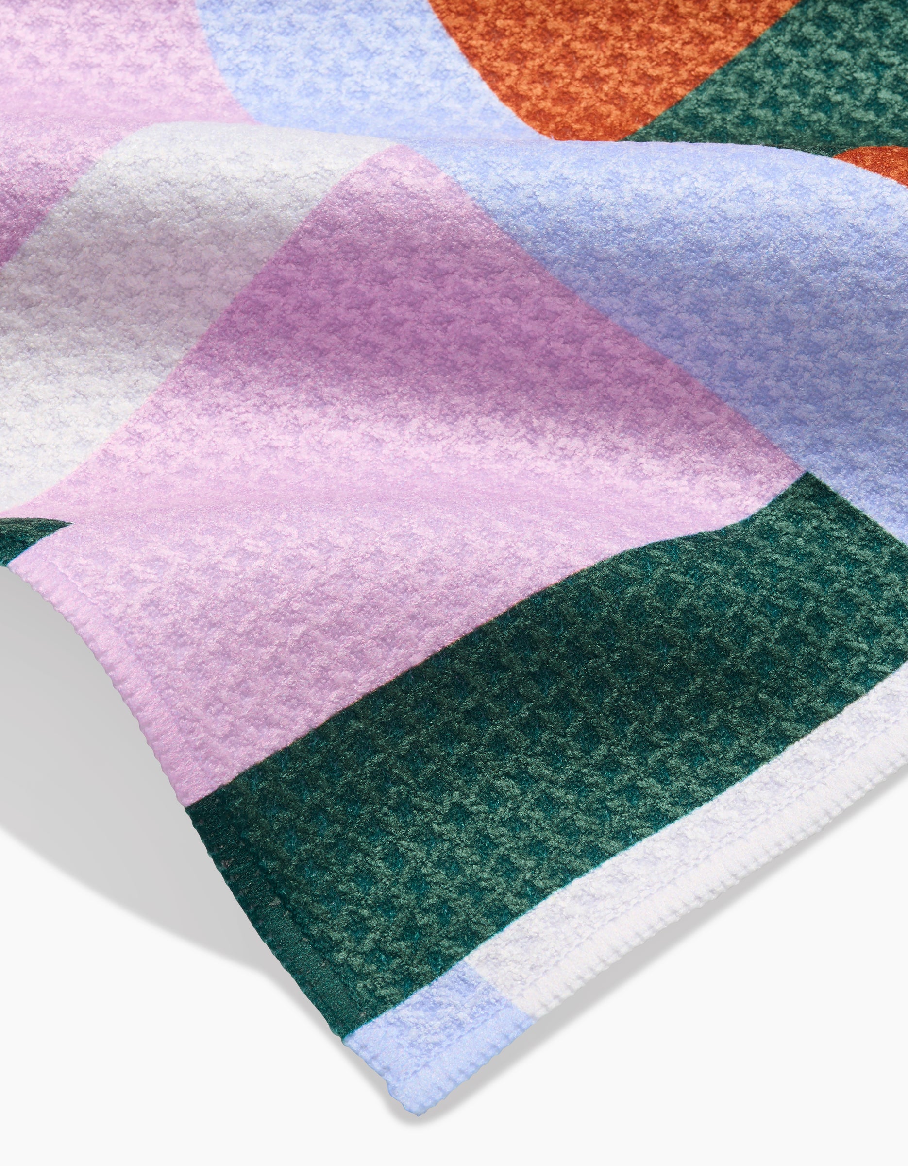 A close-up of the Claire Iglesias Abstract Collage Bar Towel, made from Geoweave fabric and featuring a geometric pattern in green, pink, purple, orange, and white with neatly sewn edges.
