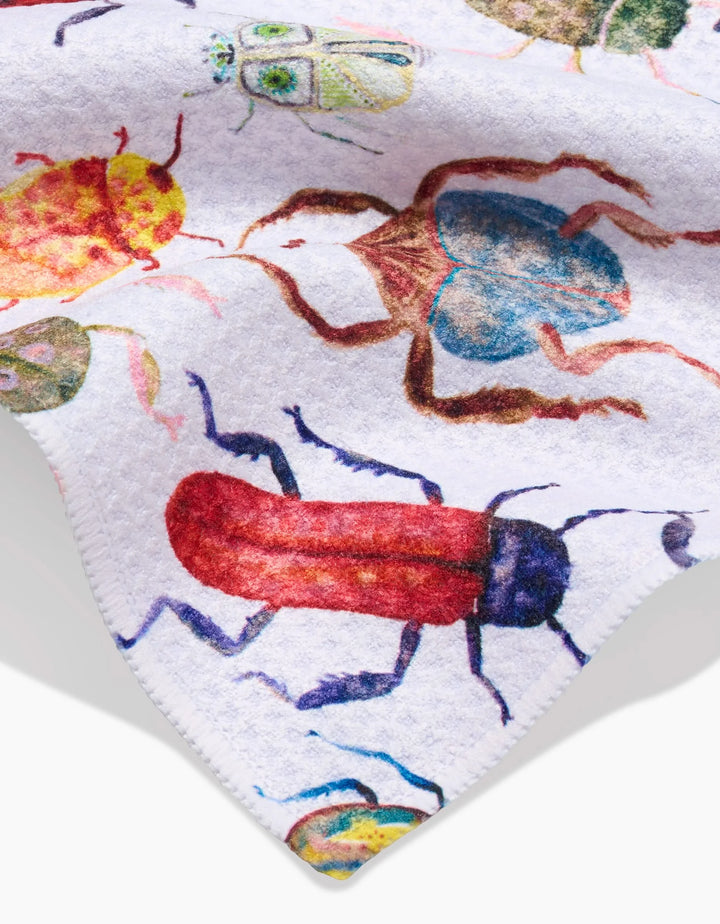 A close-up of the Taryn Brennan “African Beetles” Bar Towel, crafted from Geoweave fabric and showcasing detailed, colorful illustrations of insects in vibrant red, blue, green, and yellow tones.