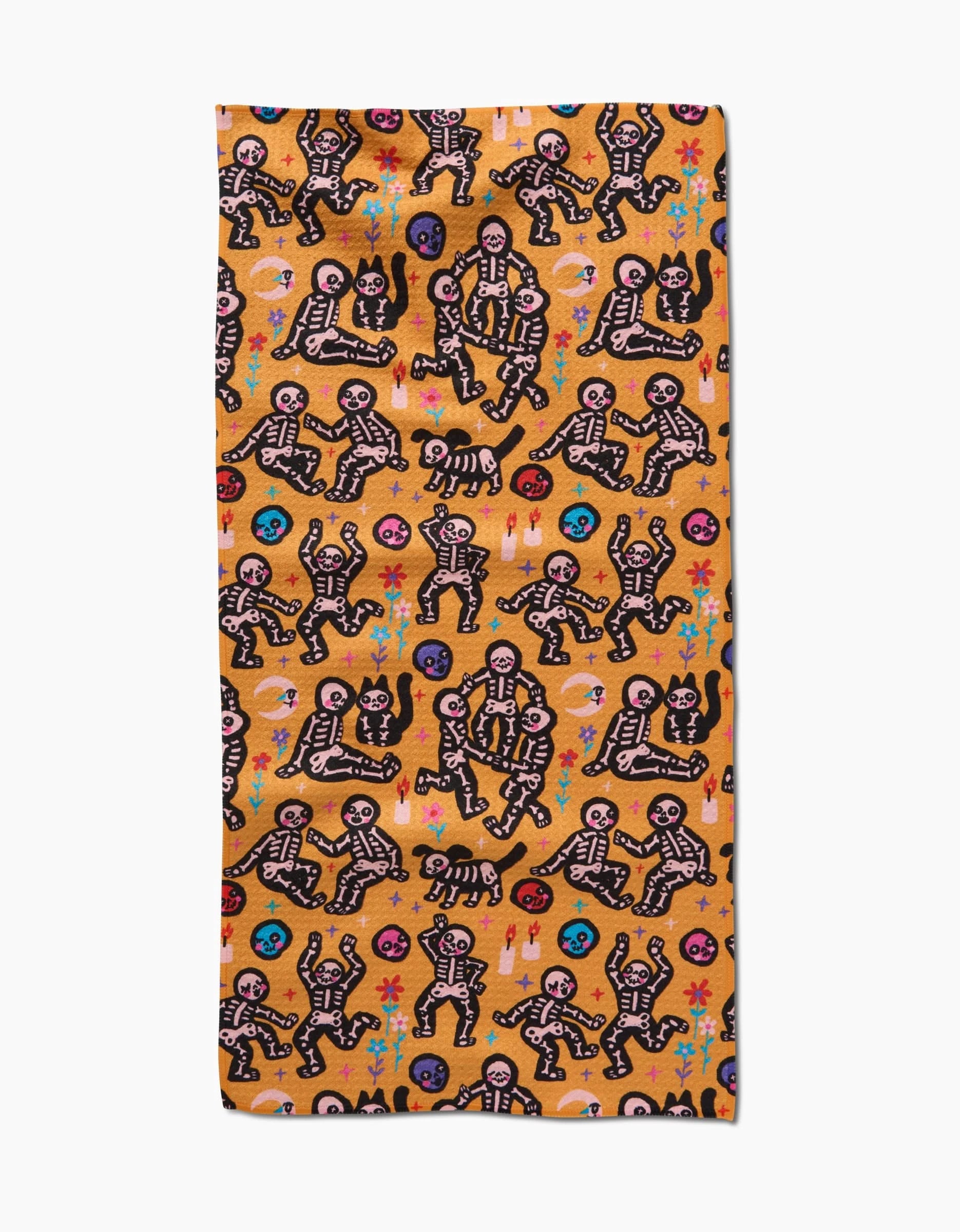 So Lazo’s After Party bar towel is made with Geoweave fabric and showcases playful black-and-white skeletons on an orange background, accented by colorful flowers, hearts, and decorative shapes.