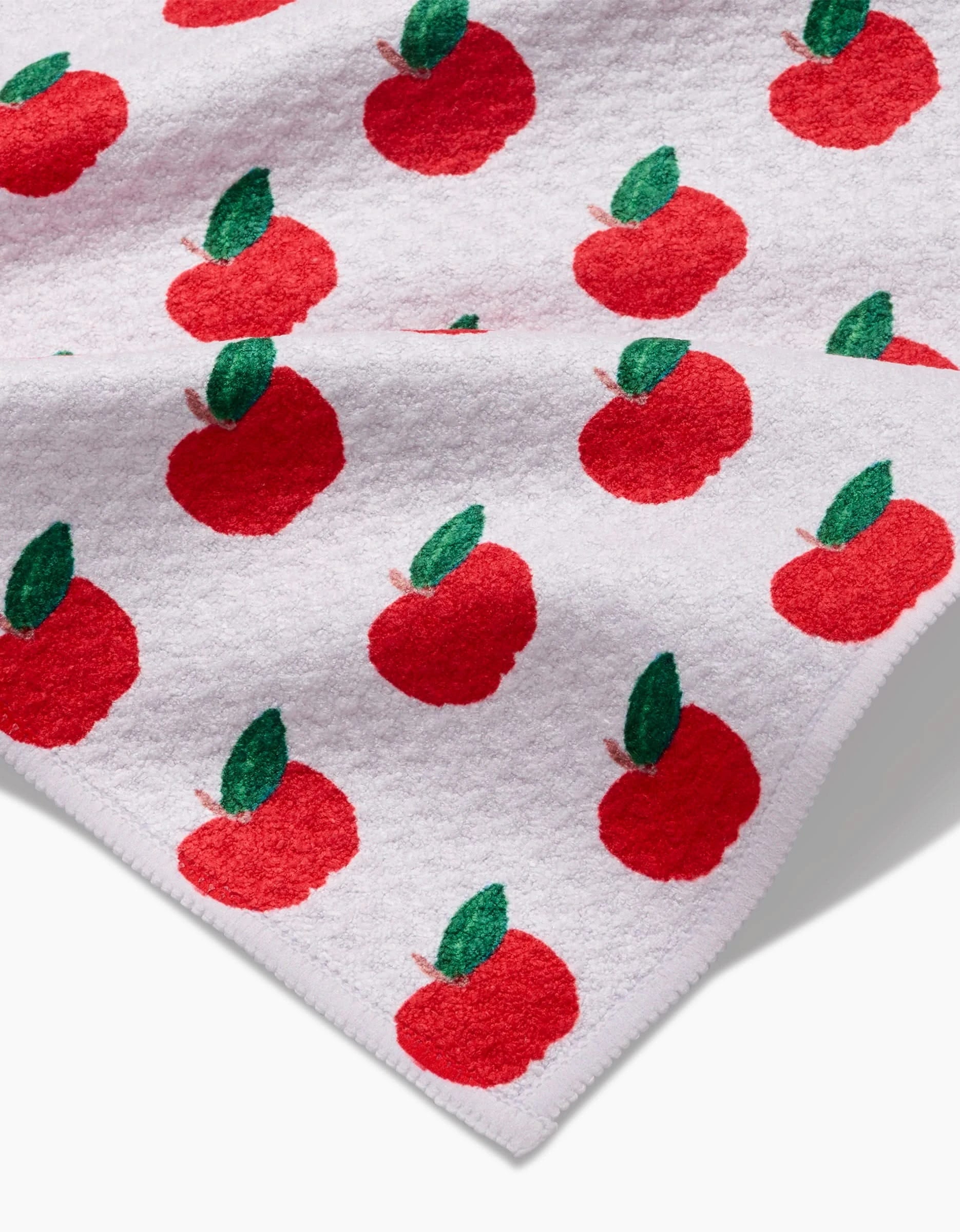 The Apple Grove bar towel by Brittany Jepsen features red apples with green leaves on ultra-absorbent Geoweave fabric, neatly folded at one corner.