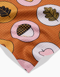The Apples Acorns towel by Megan Roy is brown, quick-drying, and soft with a repeating pattern of pink and yellow circles featuring acorns, leaves, and heart illustrations.