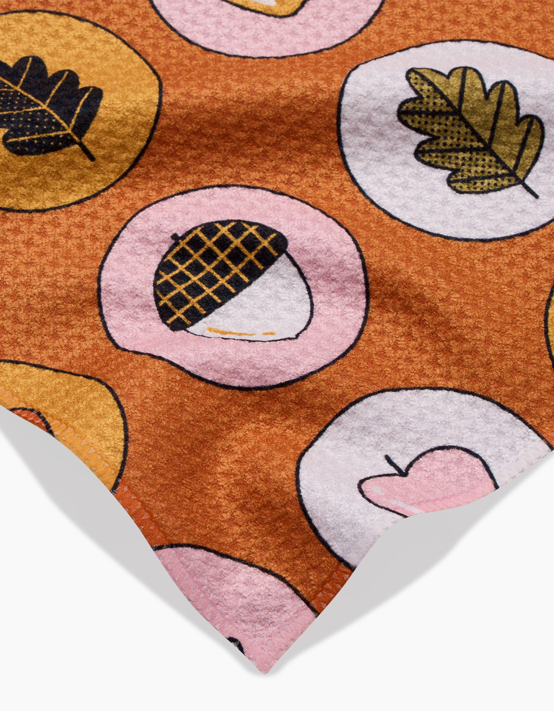 The Apples Acorns towel by Megan Roy is brown, quick-drying, and soft with a repeating pattern of pink and yellow circles featuring acorns, leaves, and heart illustrations.