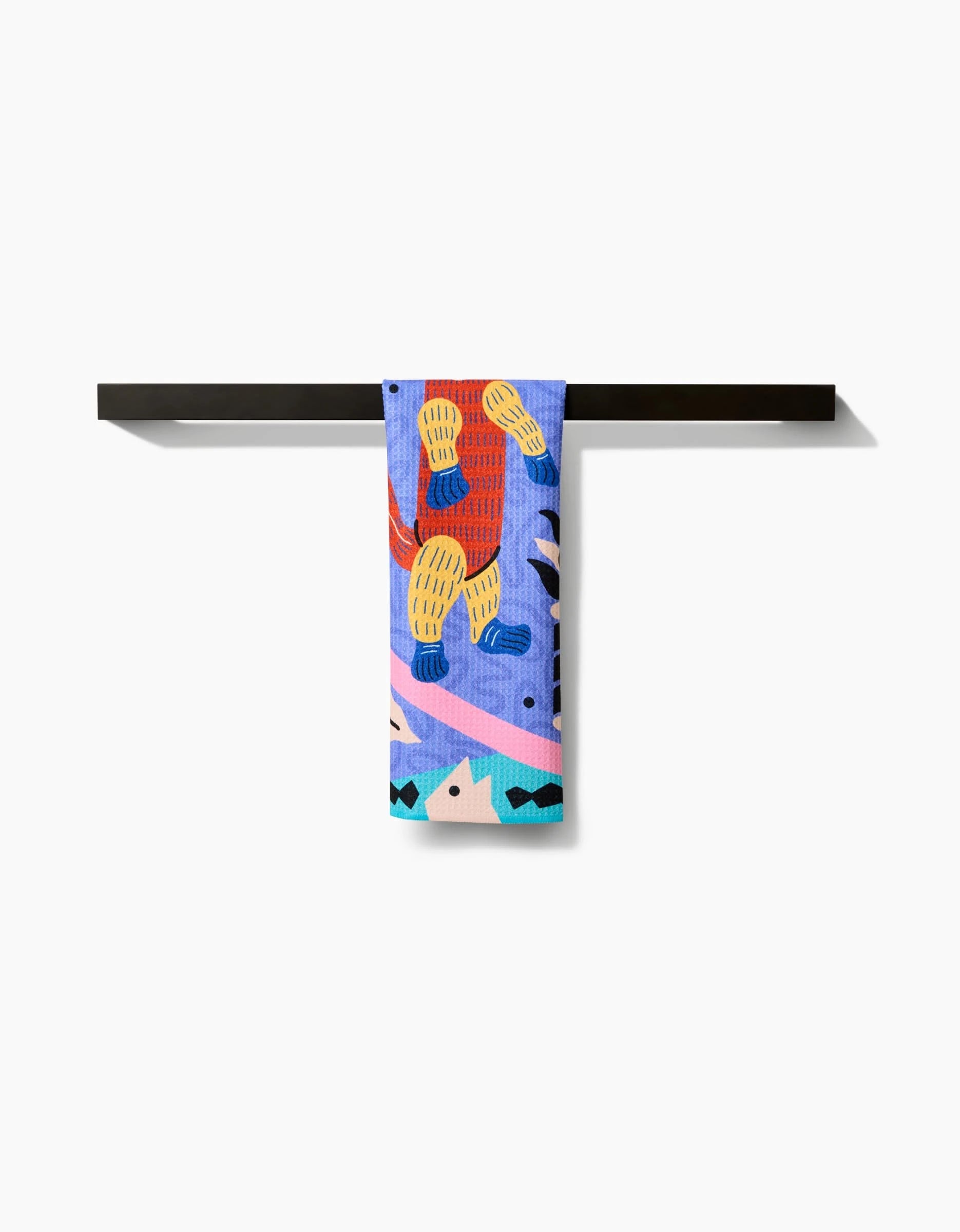 The Ariranha bar towel by Camila Leão features bold abstract patterns in blue, yellow, pink, and red. Made from ultra-absorbent Geoweave fabric, it stands out over a sleek black bar against a white background.