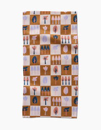 The Autumn Forest kitchen towel by Claire Iglesias is a rectangular recycled towel with a brown and beige checkered pattern, featuring stylized tree illustrations in pink, coral, navy, and light purple on each square.