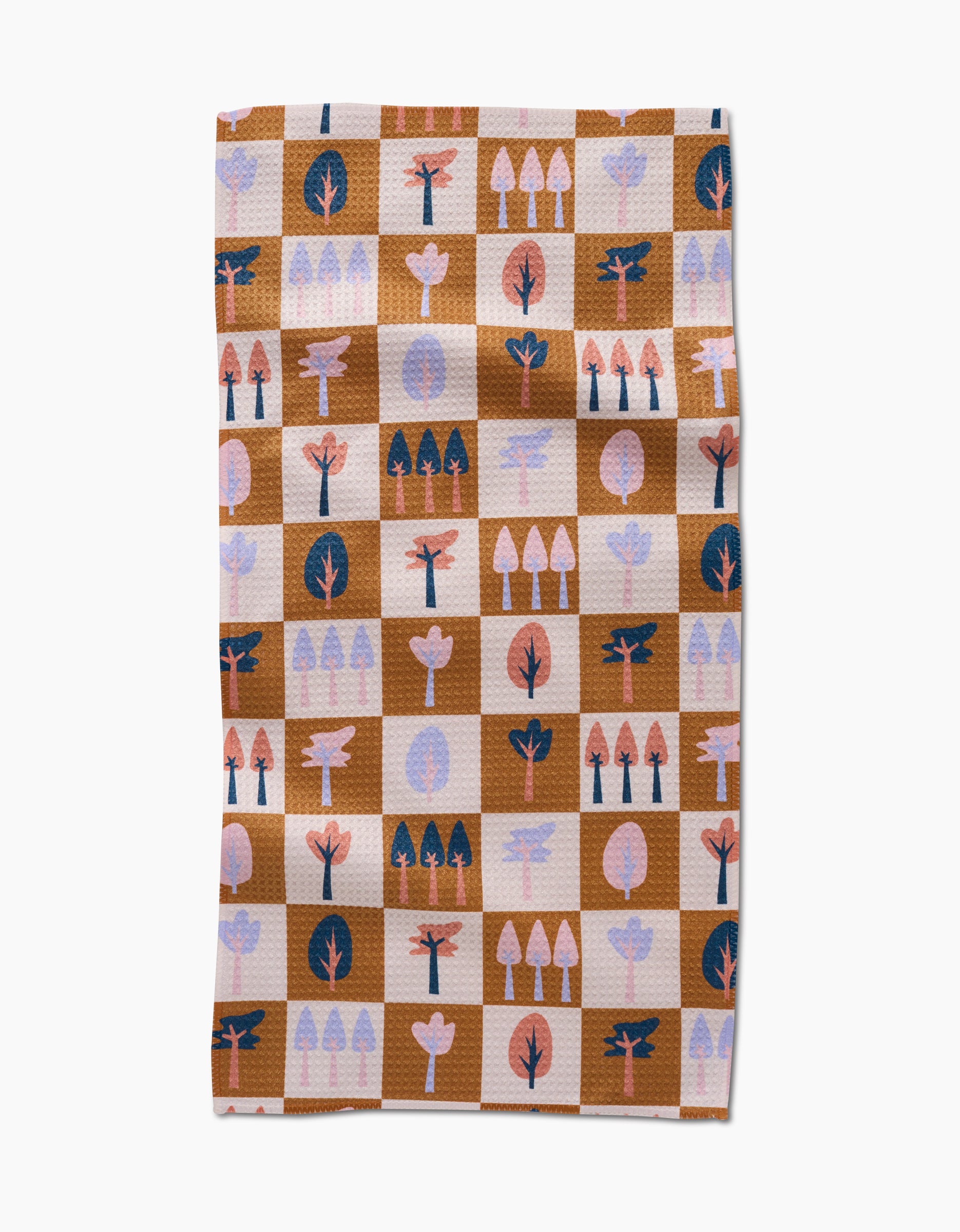 The Autumn Forest kitchen towel by Claire Iglesias is a rectangular recycled towel with a brown and beige checkered pattern, featuring stylized tree illustrations in pink, coral, navy, and light purple on each square.
