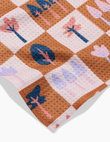 A close-up of Claire Iglesias Autumn Forest recycled kitchen towel, featuring a white and brown checkered pattern with stylized blue, pink, and purple tree and leaf illustrations in each square.