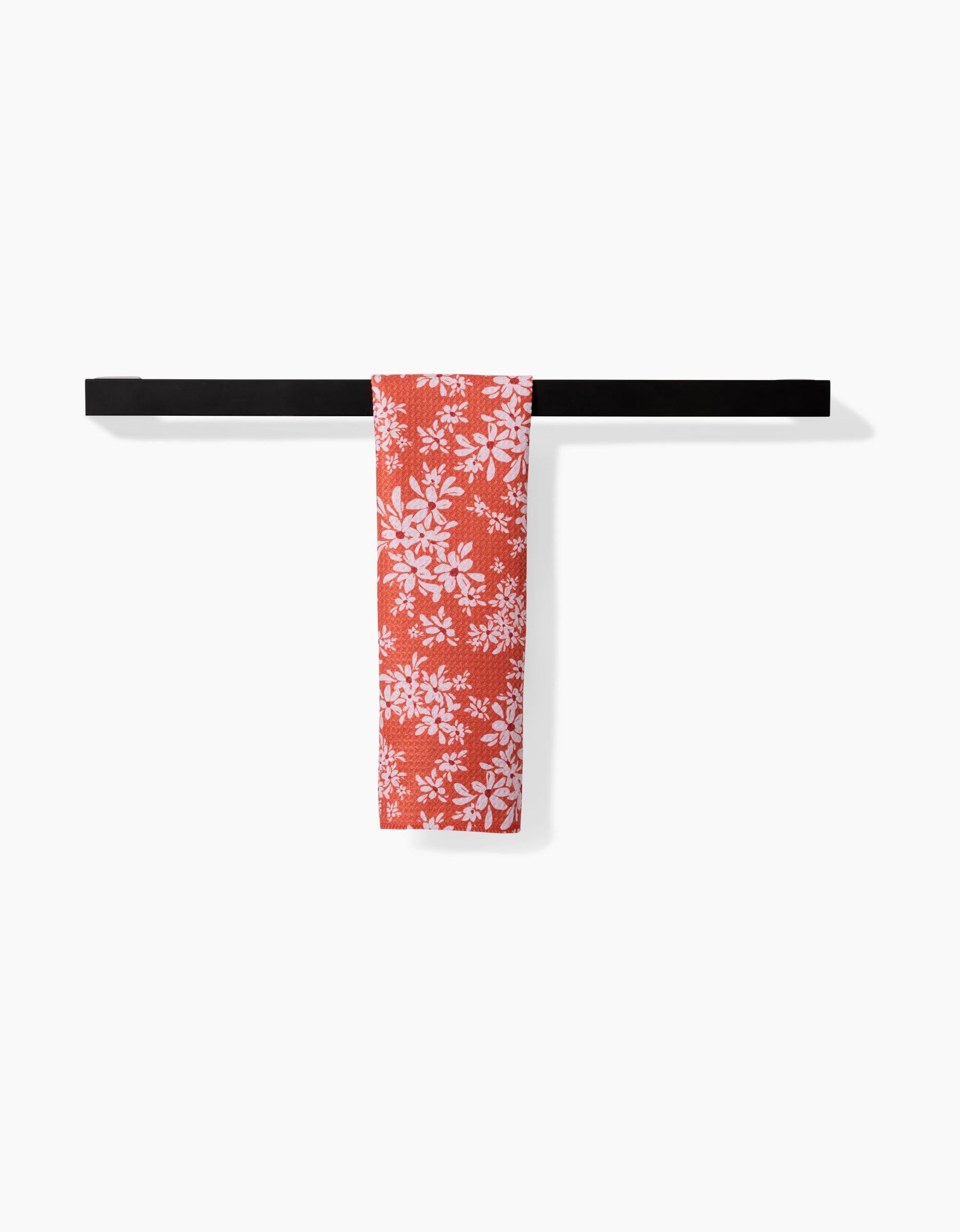 The Ashley Celena Autumn Reverie ultra-absorbent red towel, featuring a white floral pattern, is neatly folded and draped over a sleek black towel bar against a plain white background.