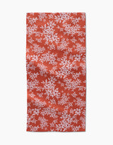 The Autumn Reverie by Ashley Celena is a red rectangular towel with a white floral pattern of scattered leaves and flowers. The ultra-absorbent fabric looks slightly wrinkled and is shown against a white background.