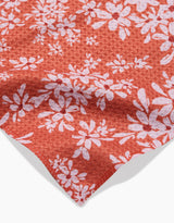 A close-up of the Ashley Celena Autumn Reverie recycled kitchen towel, showing its red fabric with a white daisy-like floral pattern and textured finish, gently folded at the corner.