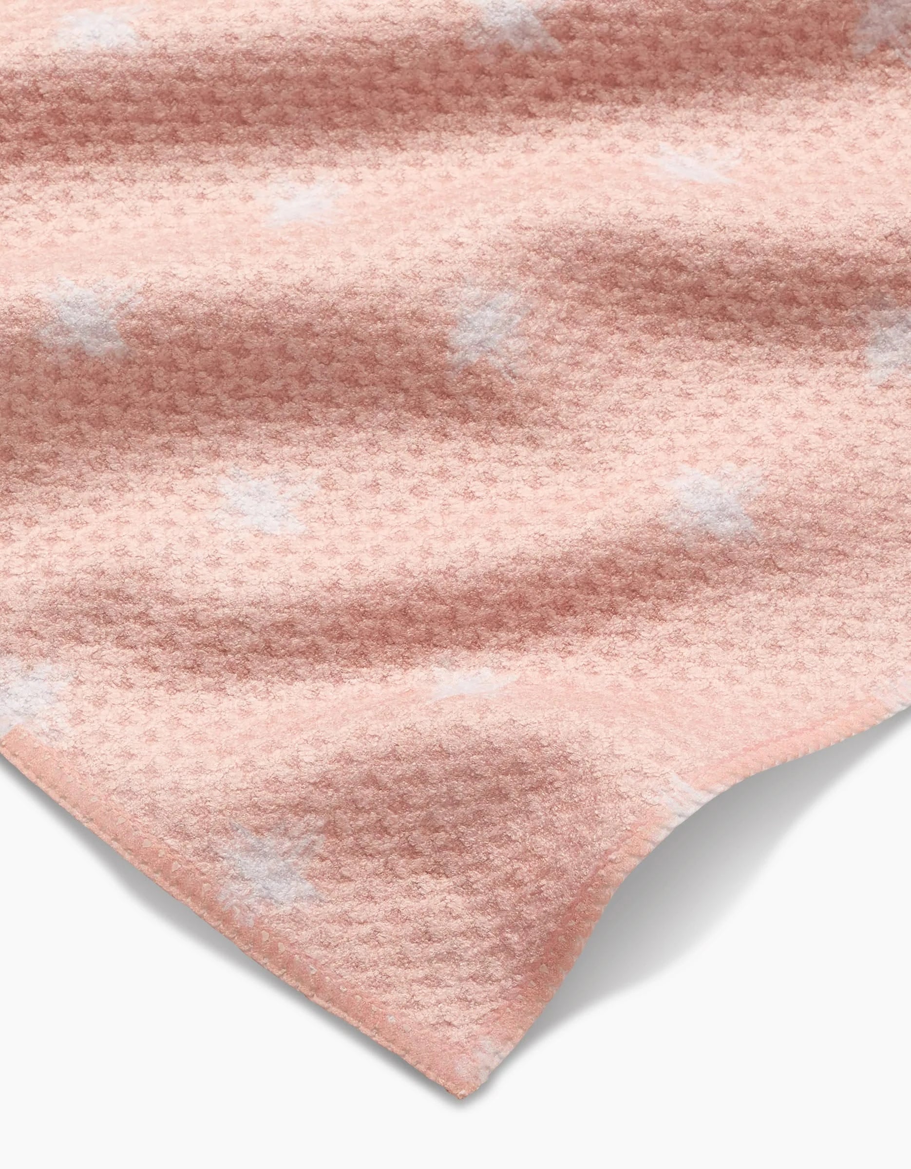 A close-up of Aveline by Amy MacCready features ultra-absorbent, soft pink Geoweave fabric with a subtle waffle texture and scattered white spots, showing gentle folds and a curved edge against a white background.