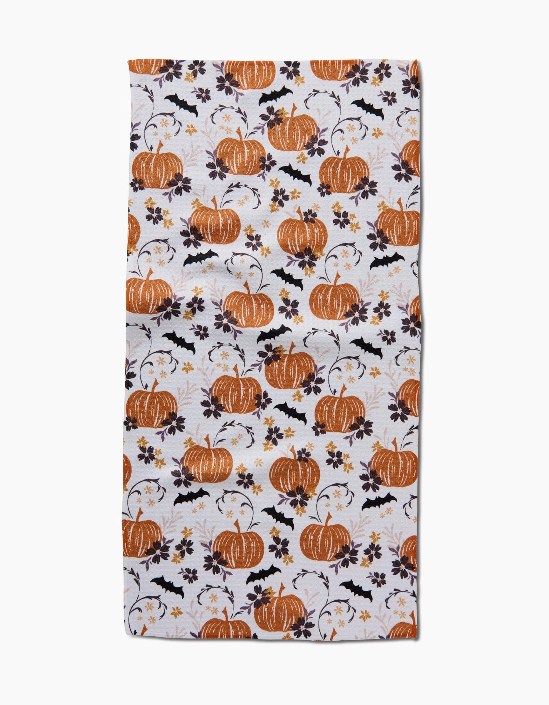 The Bats In The Pumpkin Patch bar towel by Ashley Celena is a rectangular, ultra-absorbent white towel with orange pumpkins, black leaves, bats, and yellow flowers for a festive autumn kitchen accent.
