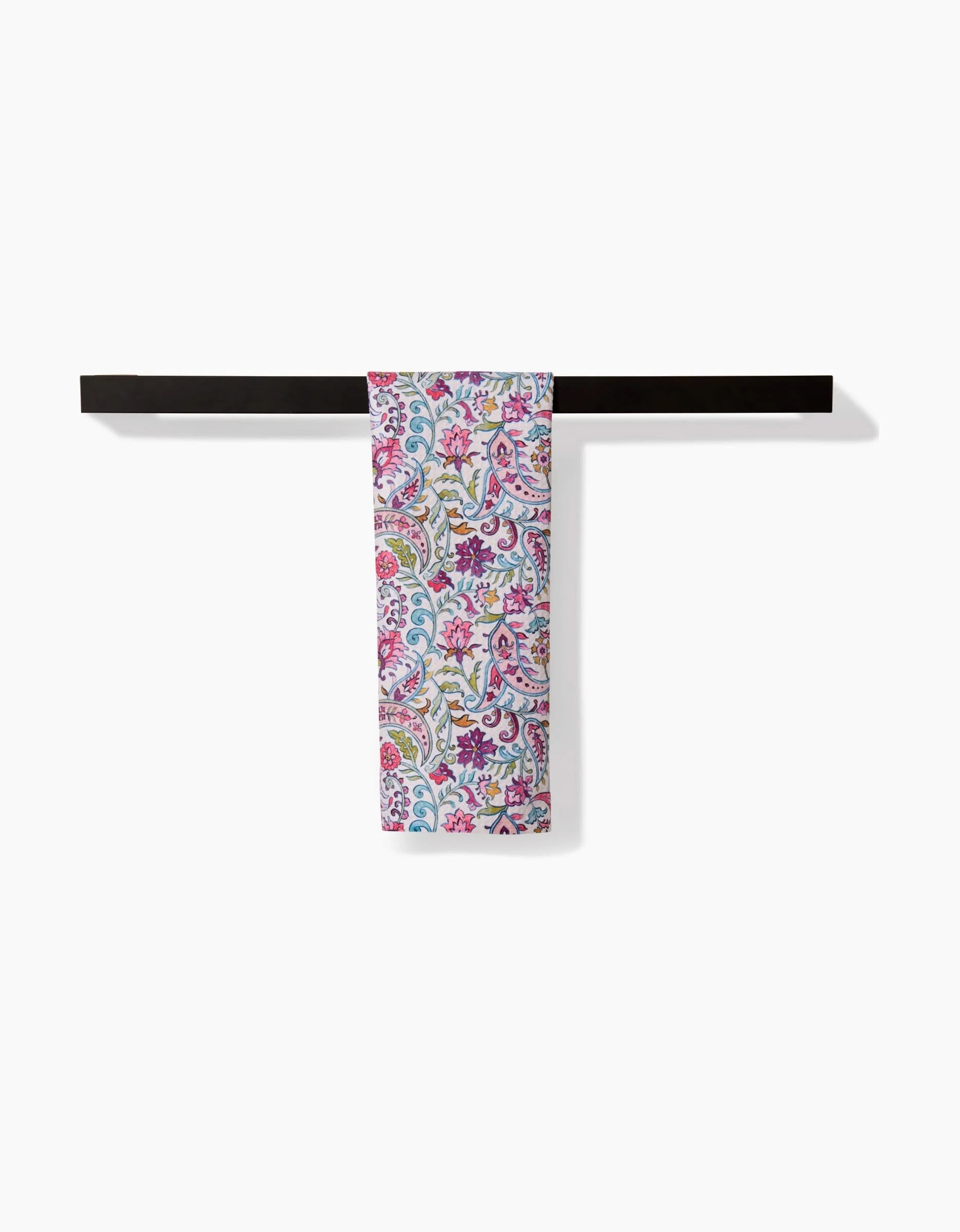 The Bazaar towel by Maayan Alper-Swan, featuring pink, yellow, and blue floral patterns, hangs neatly folded over a sleek black bar towel rack against a plain white background.