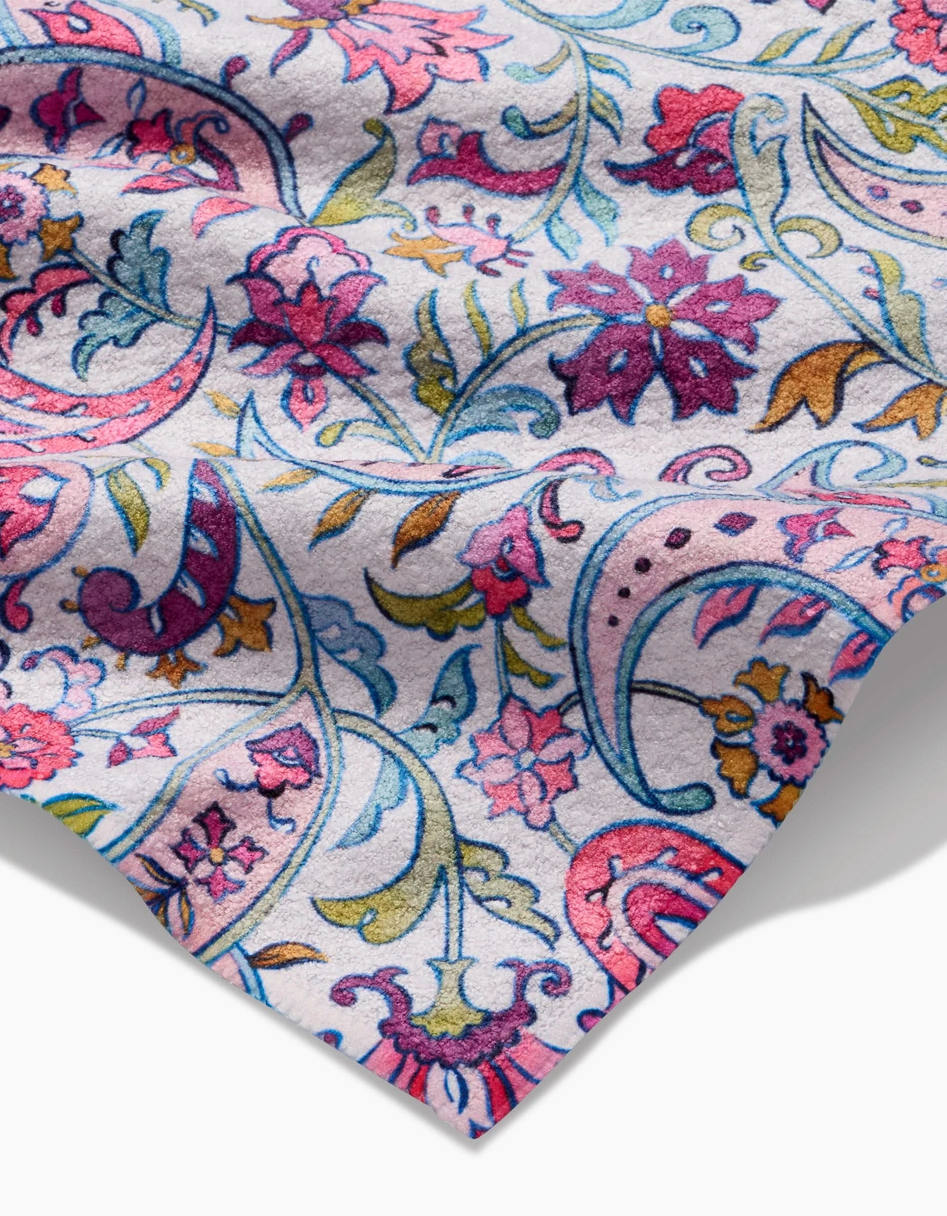 A close-up of the Bazaar bar towel by Maayan Alper-Swan, featuring ultra-absorbent Geoweave fabric with a vibrant floral and paisley pattern in pink, purple, blue, yellow, and green on a light background. The towel is slightly wrinkled at the edge.