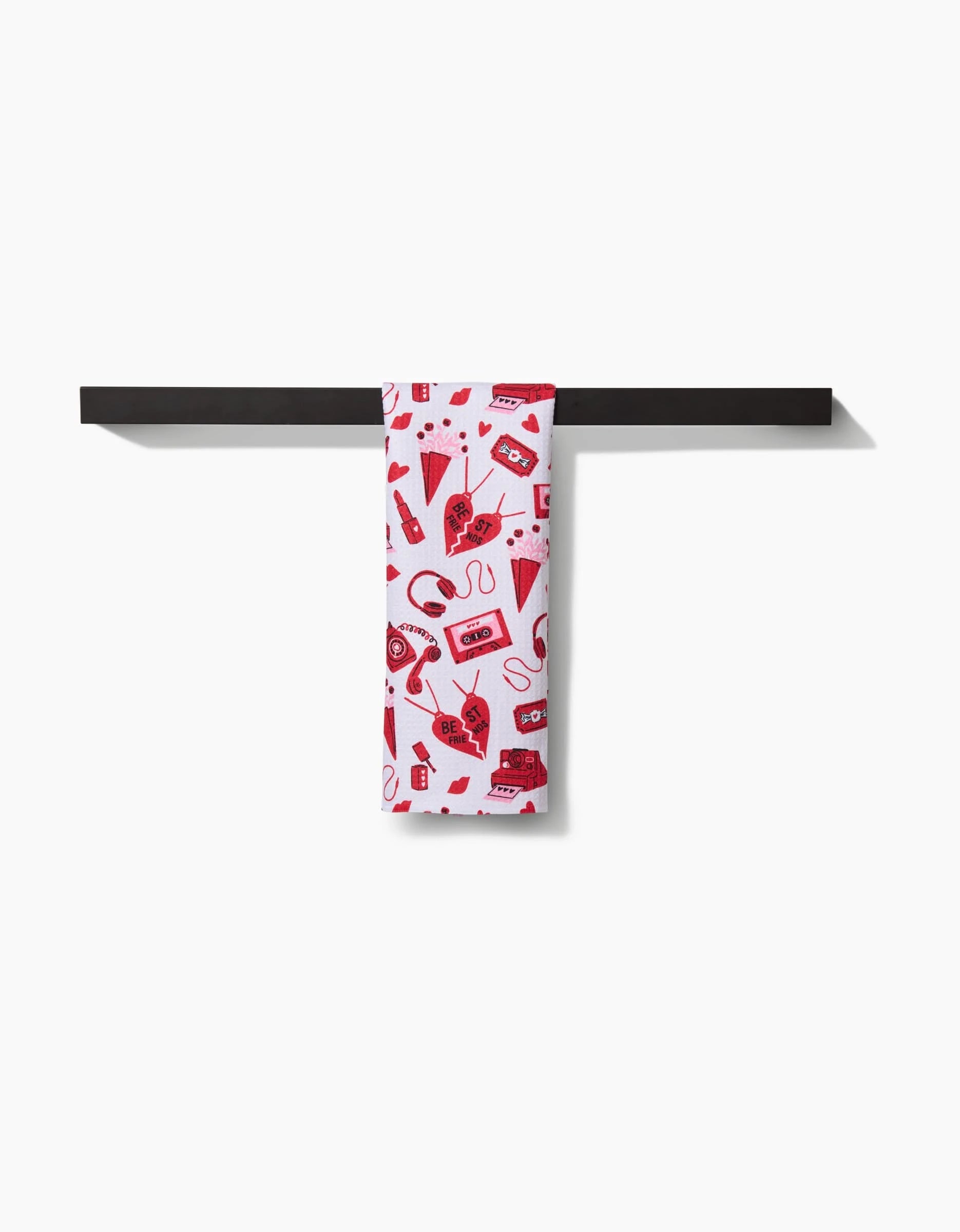 The Best Friends towel by Charlie Rowan Designs, featuring red retro illustrations on ultra-absorbent white fabric, is neatly draped over a black bar against a plain white background.