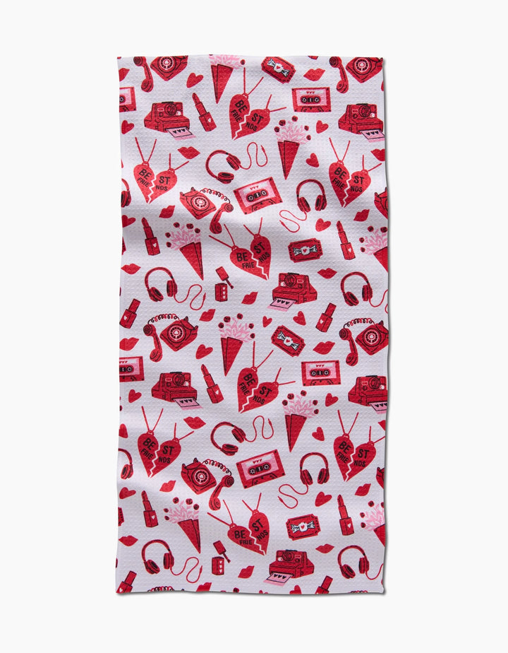 The Best Friends rectangular bar towel by Charlie Rowan Designs features a repeating red and pink pattern of hearts, cassette tapes, radios, headphones, soda bottles, and envelopes on white. Ultra-absorbent—fun and functional!.