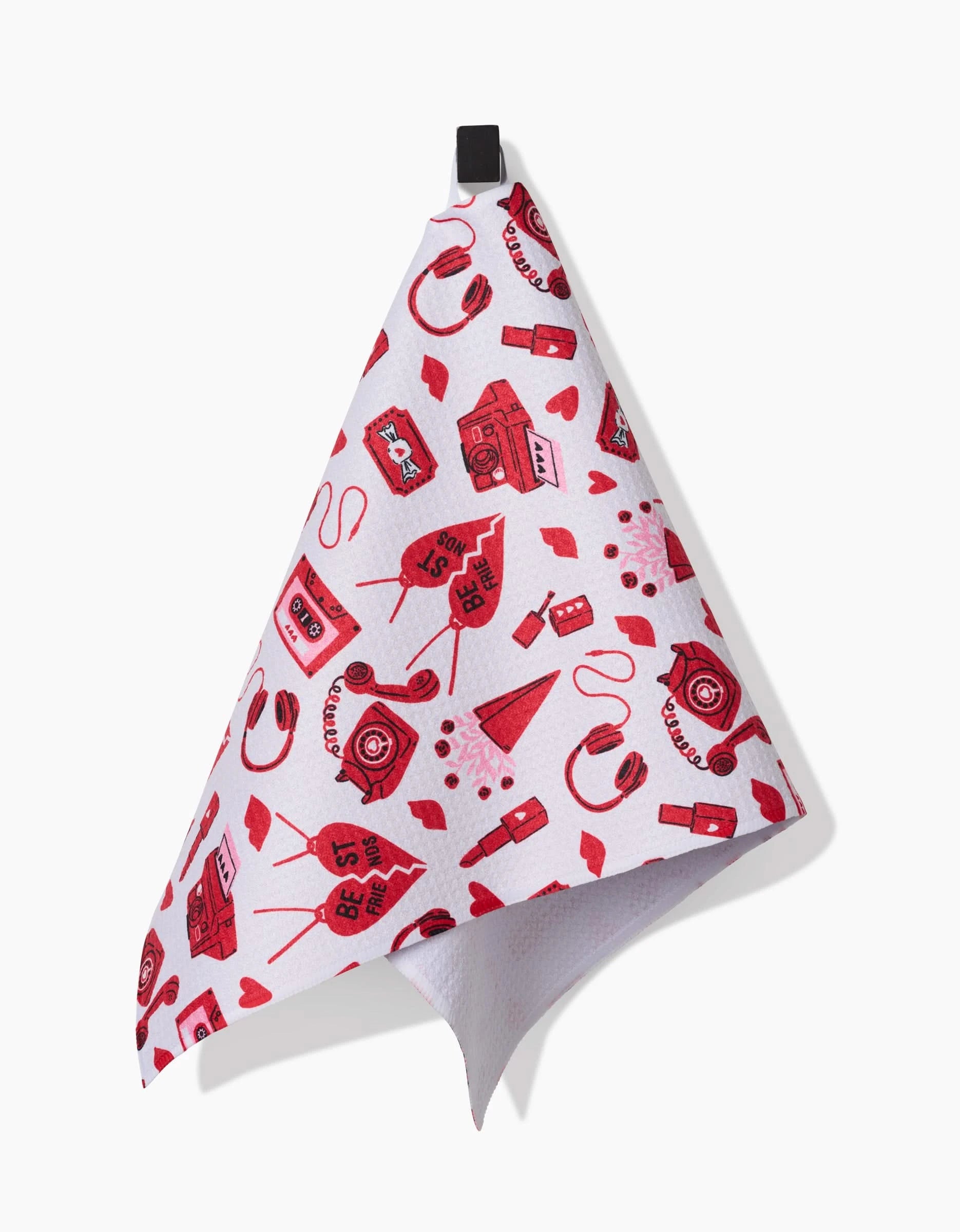 The Best Friends kitchen towel by Charlie Rowan Designs is white with a black loop and red illustrations of cassette tapes, cameras, headphones, paper airplanes, hearts, and speech bubbles with BFF and Best.