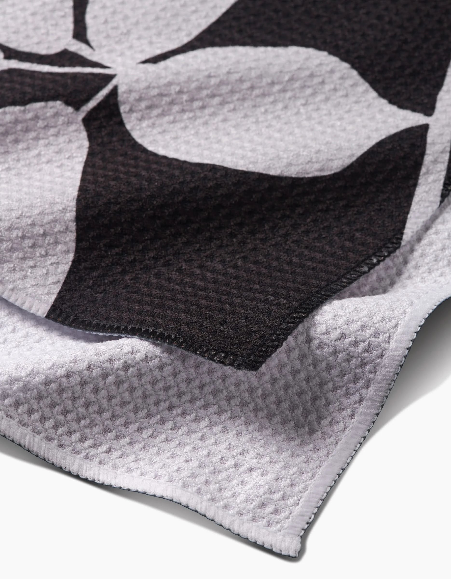 A close-up of the PrintedPlant Blackberry bar towel featuring Geoweave fabric, a bold black and white floral print, detailed edge stitching, and a textured waffle-like surface.