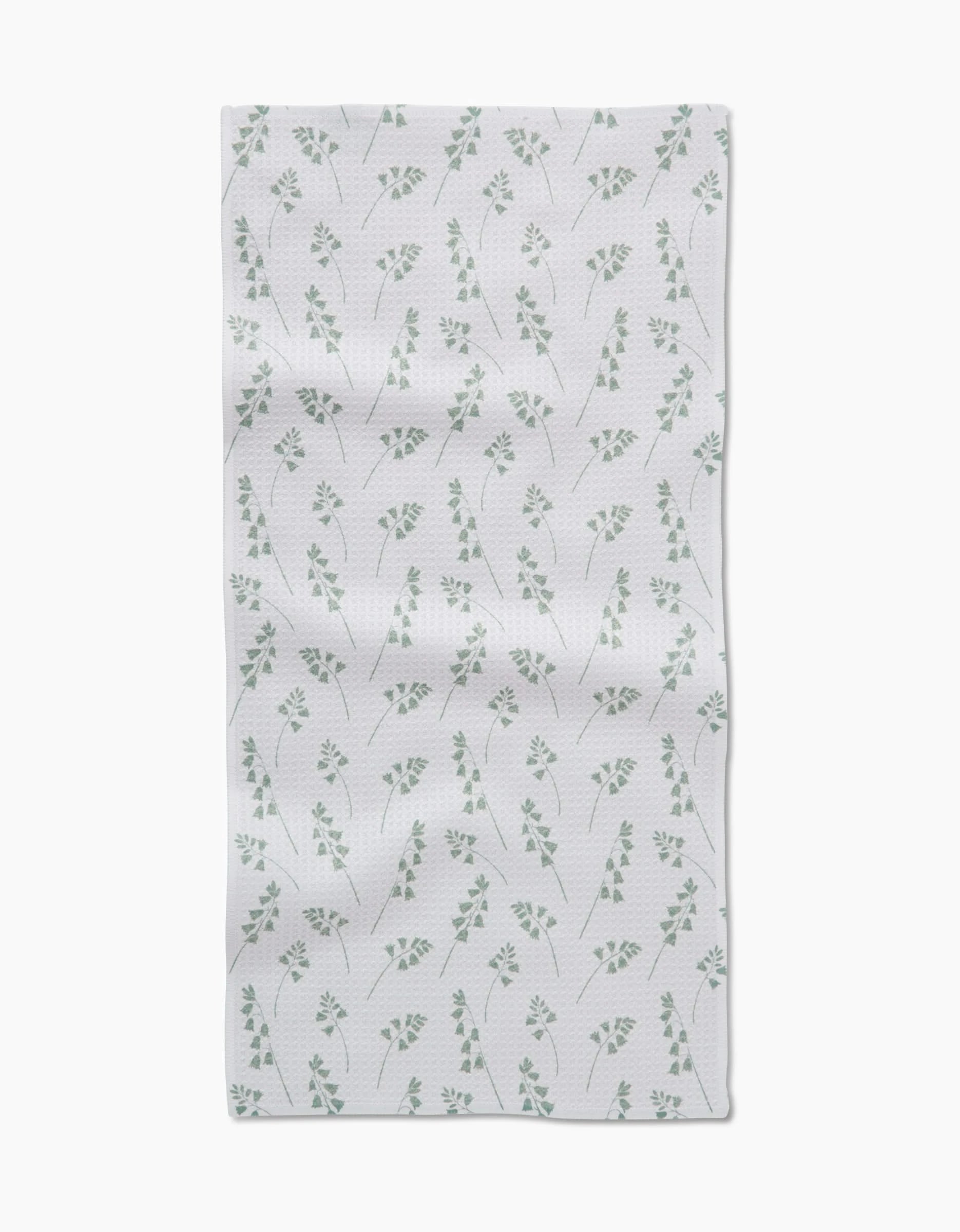 The Linda Fox Blue Bells Green Bar Towel features a Geoweave fabric with a subtle pattern of small green leaves and branches, evenly spaced on a white background, and a slight wrinkled texture for added charm.