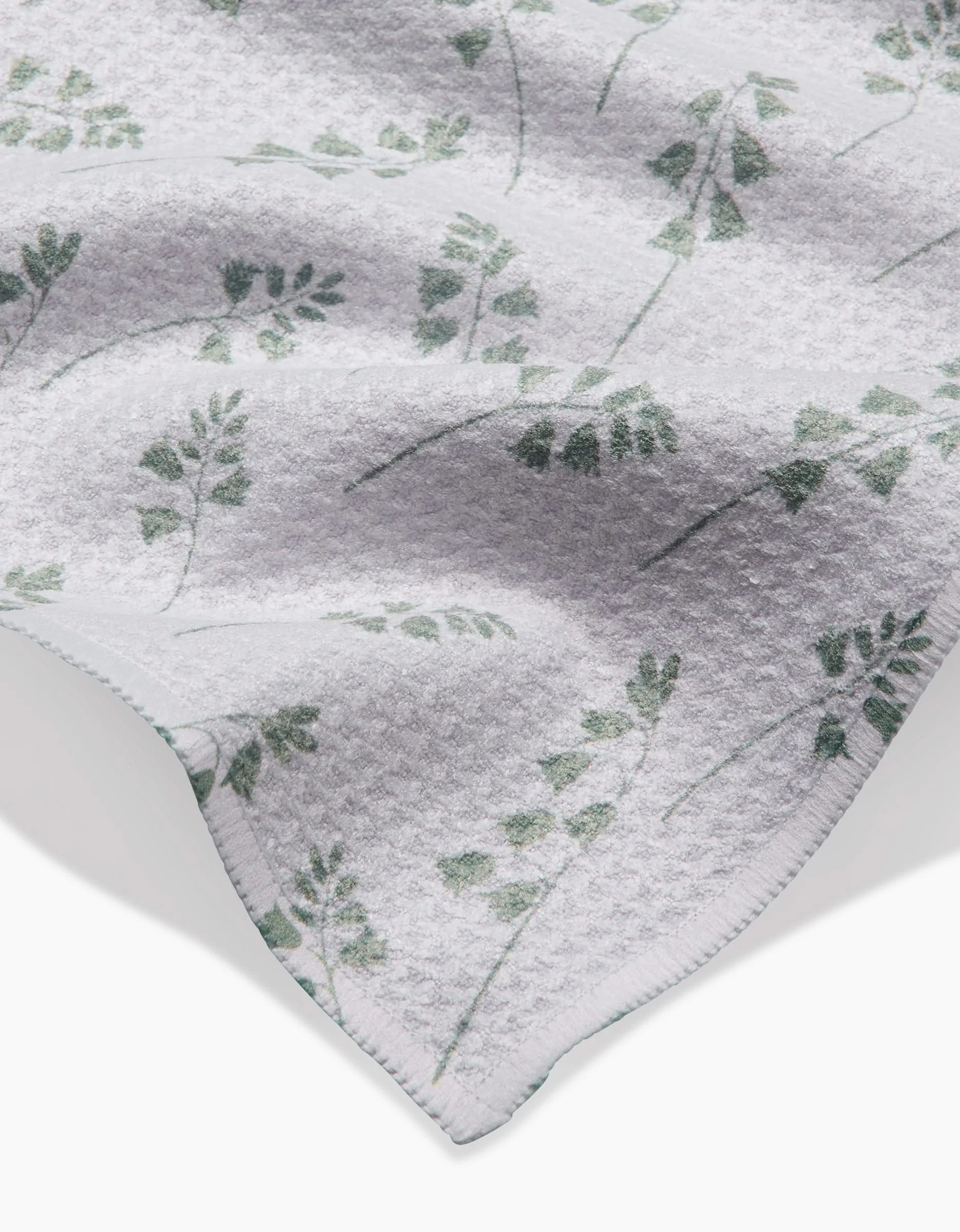 A close-up of the Linda Fox Blue Bells Green Geoweave bar towel in white, featuring a subtle green leafy branch pattern and a visible, neatly stitched hem.
