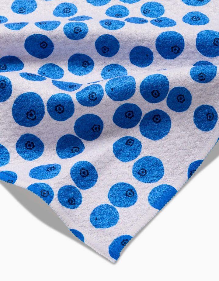 The Bluebs Bar Towel by Brittany Jepsen features a repeating bright blue circle pattern with simple designs on a white Geoweave fabric, partially folded to highlight its texture.