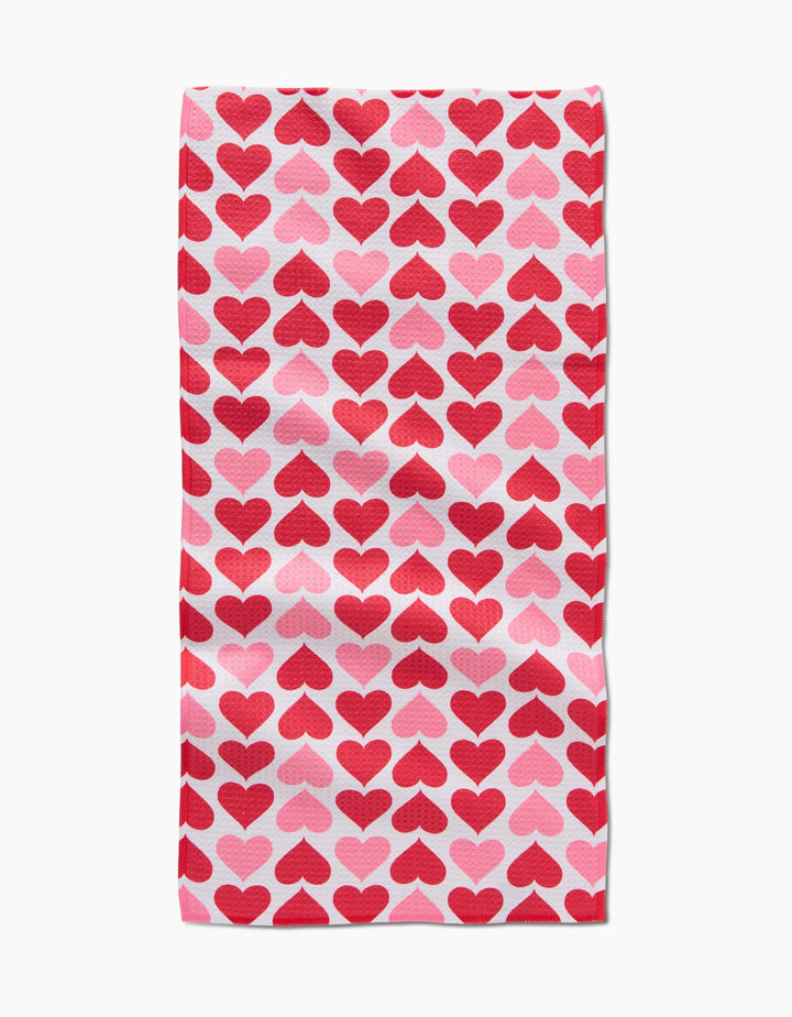 The Blushing Hearts bar towel by Danelys Sidron is made from recycled materials and showcases a white background with red and pink hearts, arranged in neat, evenly spaced rows and columns.