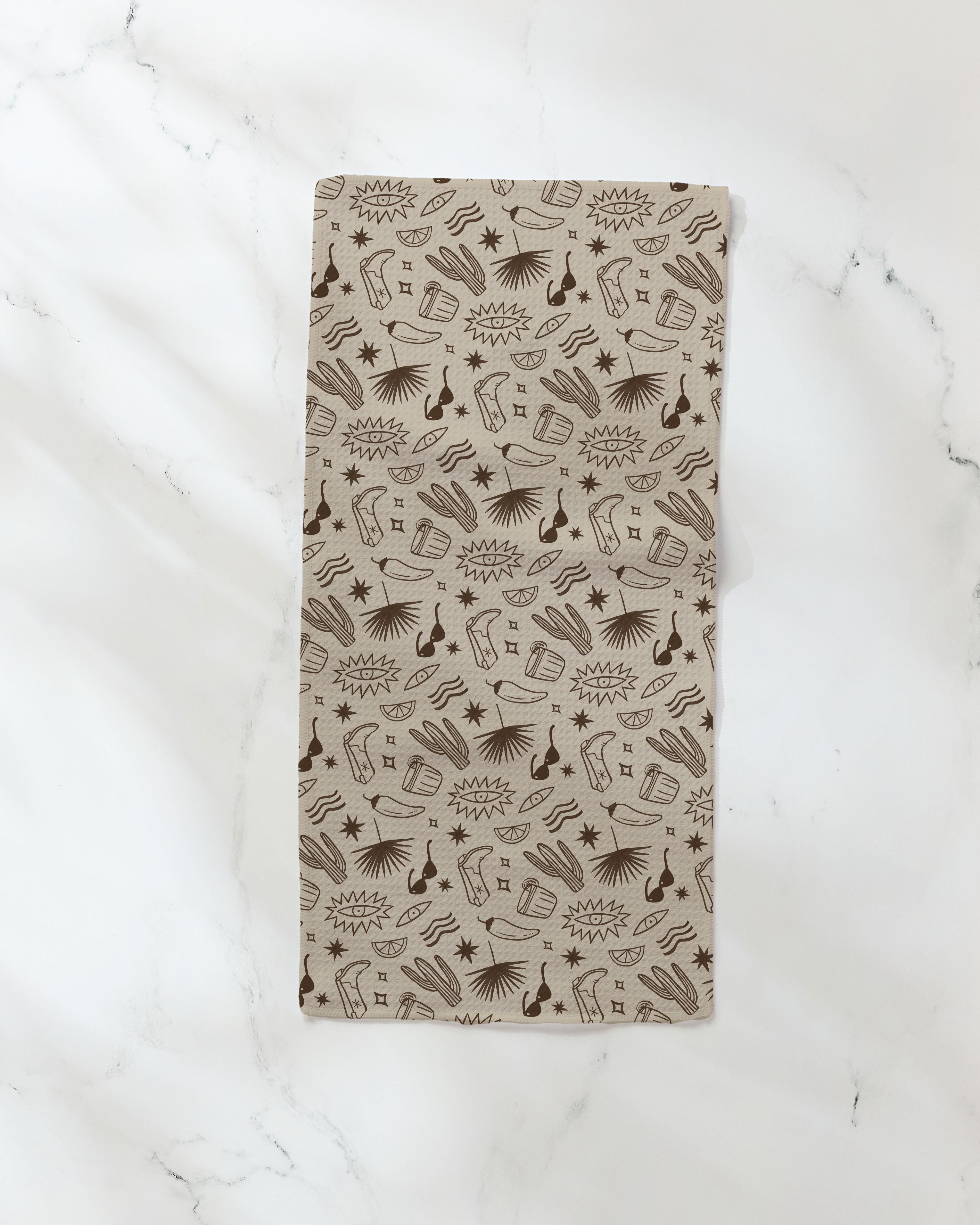The Bonfire Nights bar towel by Geometry, featuring brown comic-style guitars, microphones, notes, stars, and sound bursts on beige fabric, is displayed on a white marble surface.