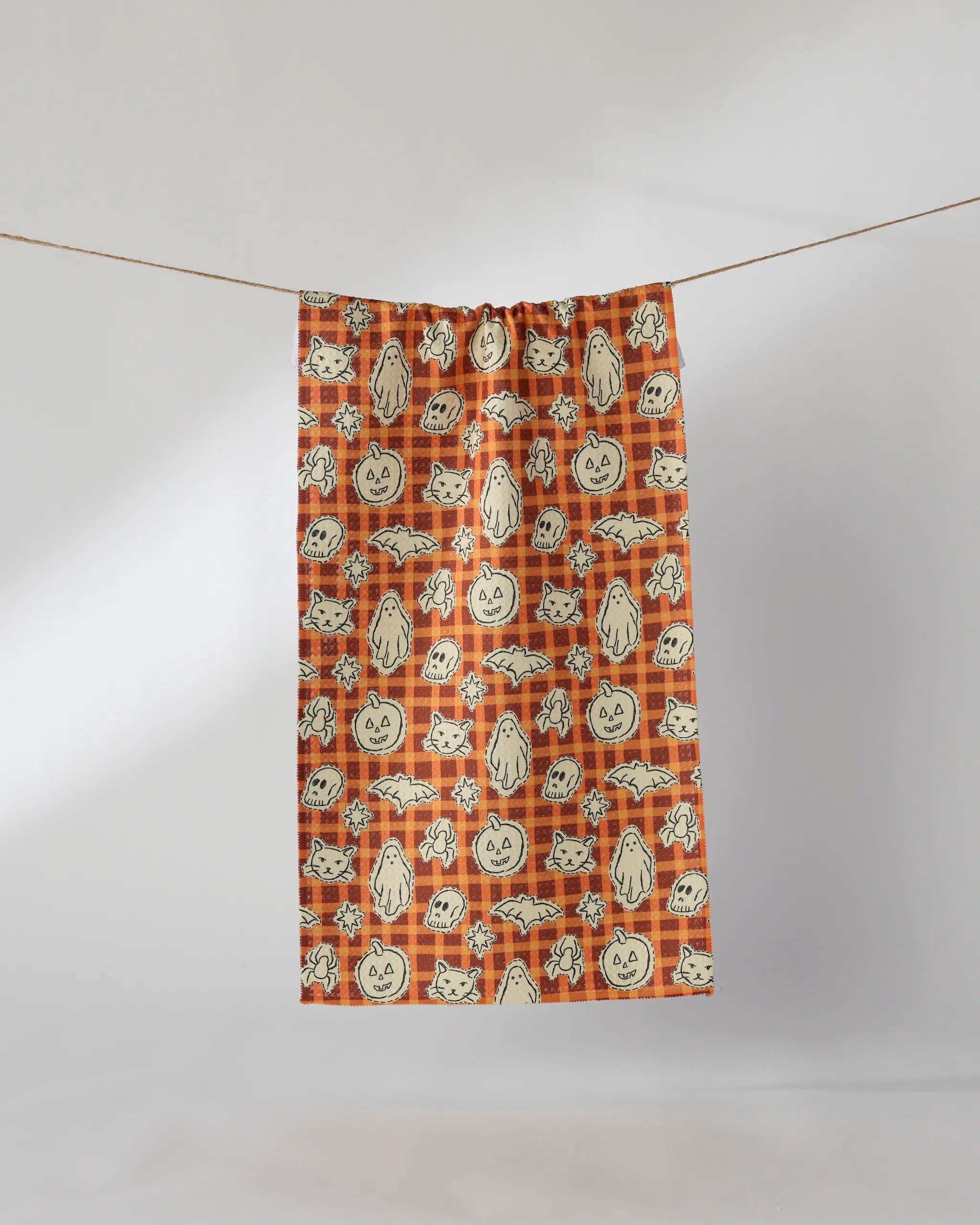 The Geometry "Boo Crew" bar towel features a playful Halloween pattern with ghosts, bats, jack-o’-lanterns, and cats on an orange plaid background. Ultra-absorbent and perfect for festive decor, it hangs easily on a line.