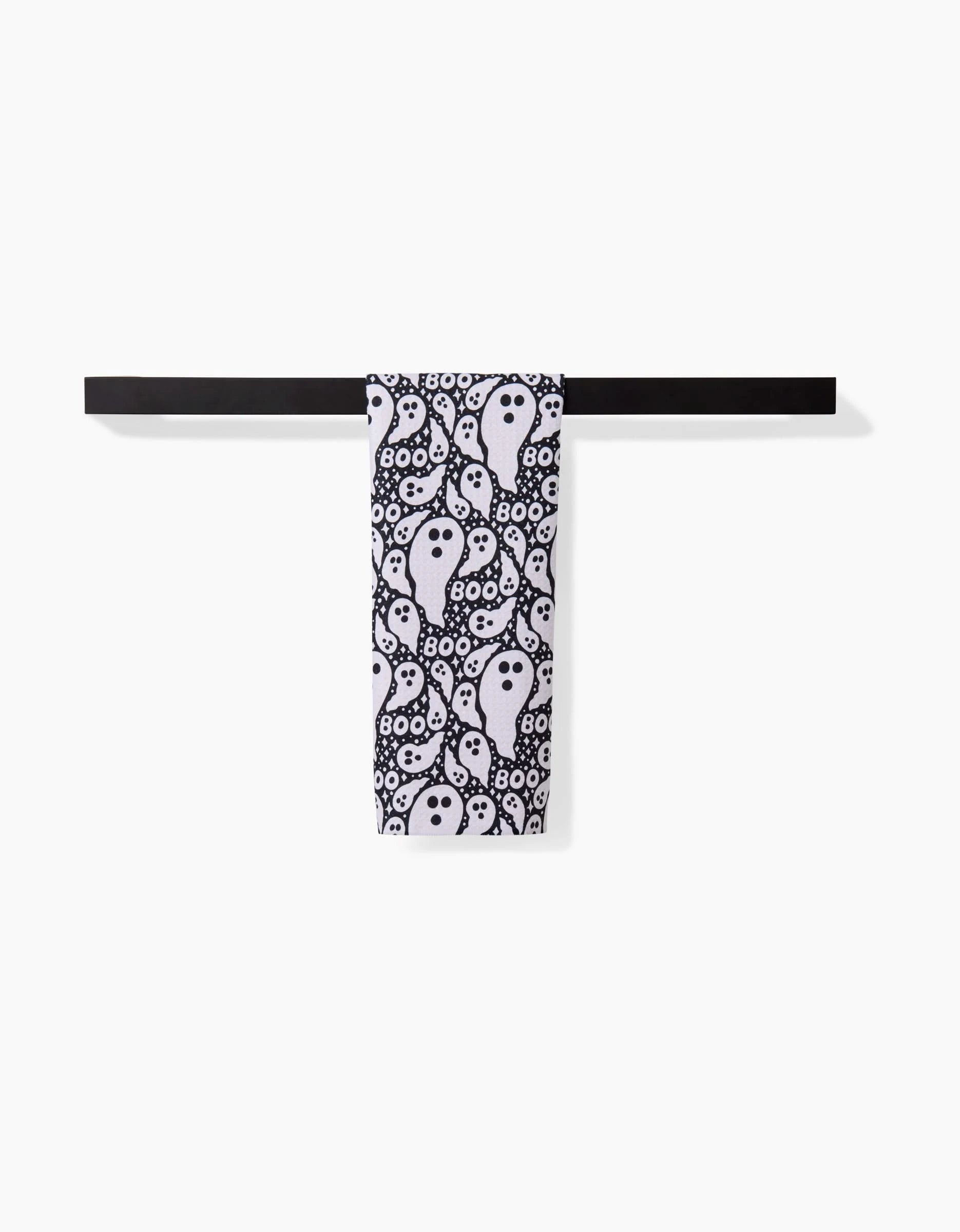A Rosa Kichline Boo Ghosts black towel rack holds an ultra-absorbent bar towel with a white base, covered in repeating black and white ghost and eyeball designs, set against a plain white background.