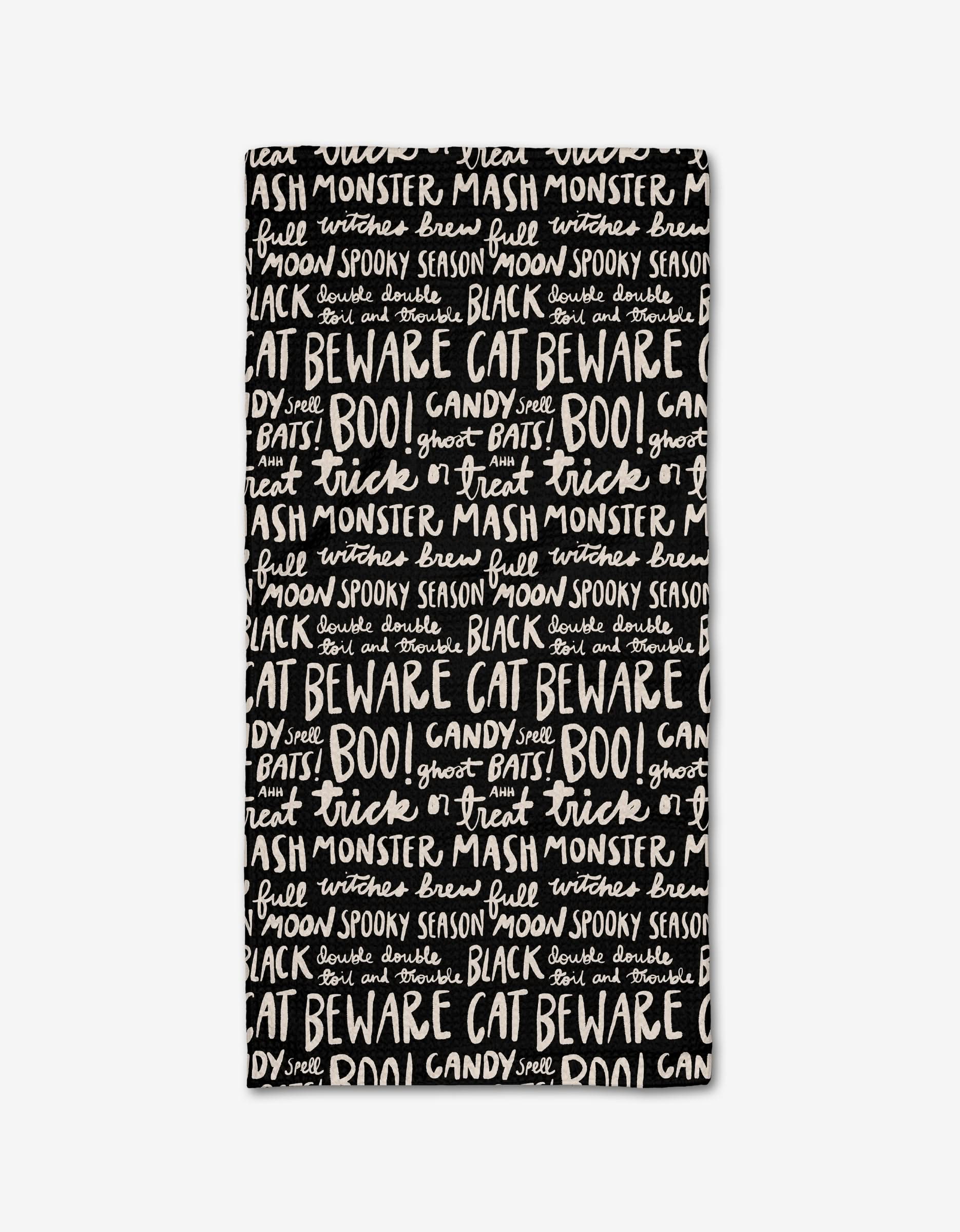 The Booos Bar Towel by Kayla Ann is a rectangular black towel made from recycled materials, decorated with playful white handwritten-style Halloween phrases like BOO!, BEWARE, trick or treat, and monster mash.