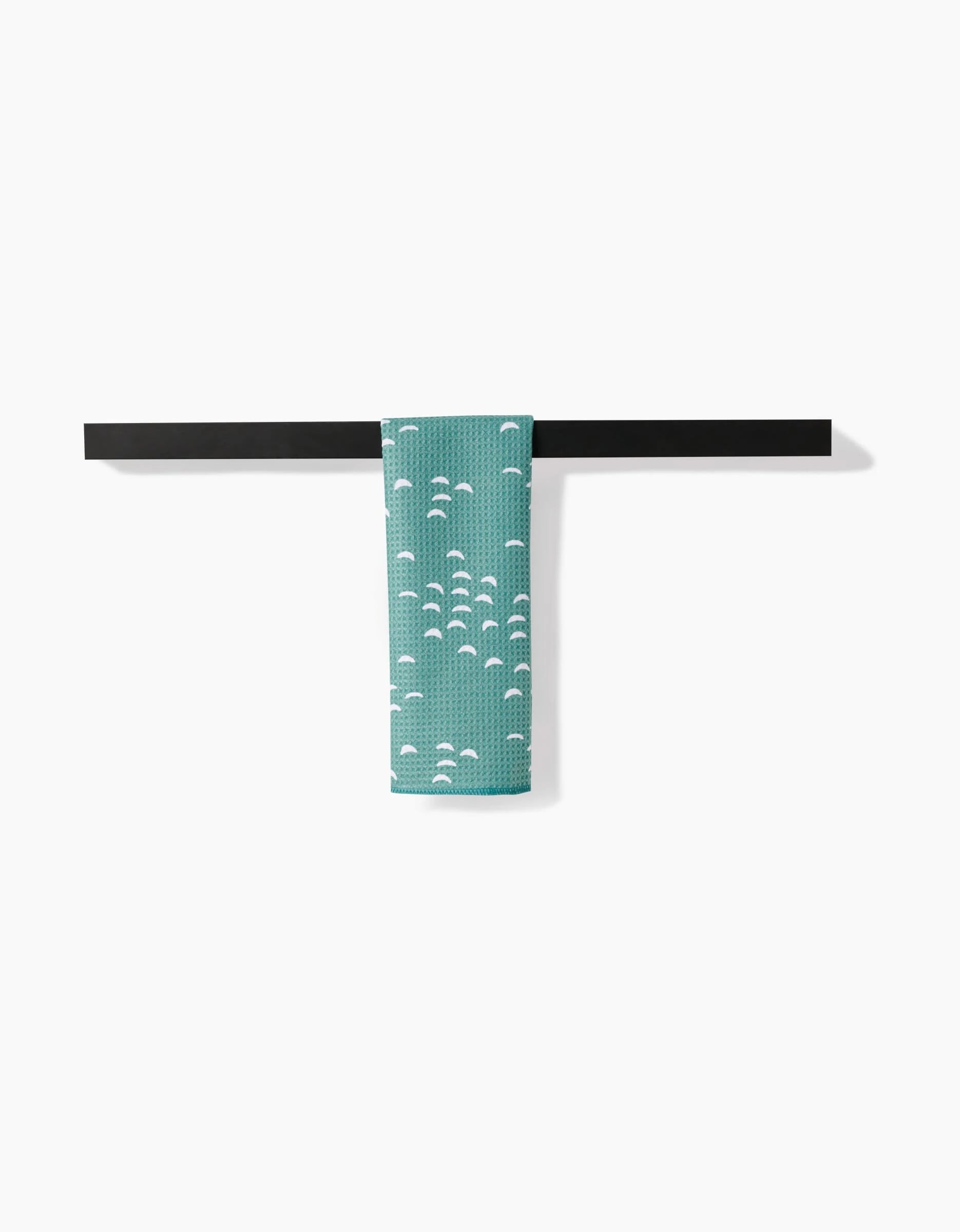 The Jessica Swift Breezeway teal bar towel, featuring a white semicircle pattern and crafted from Geoweave fabric, is neatly folded over a simple black towel bar against a plain white background.