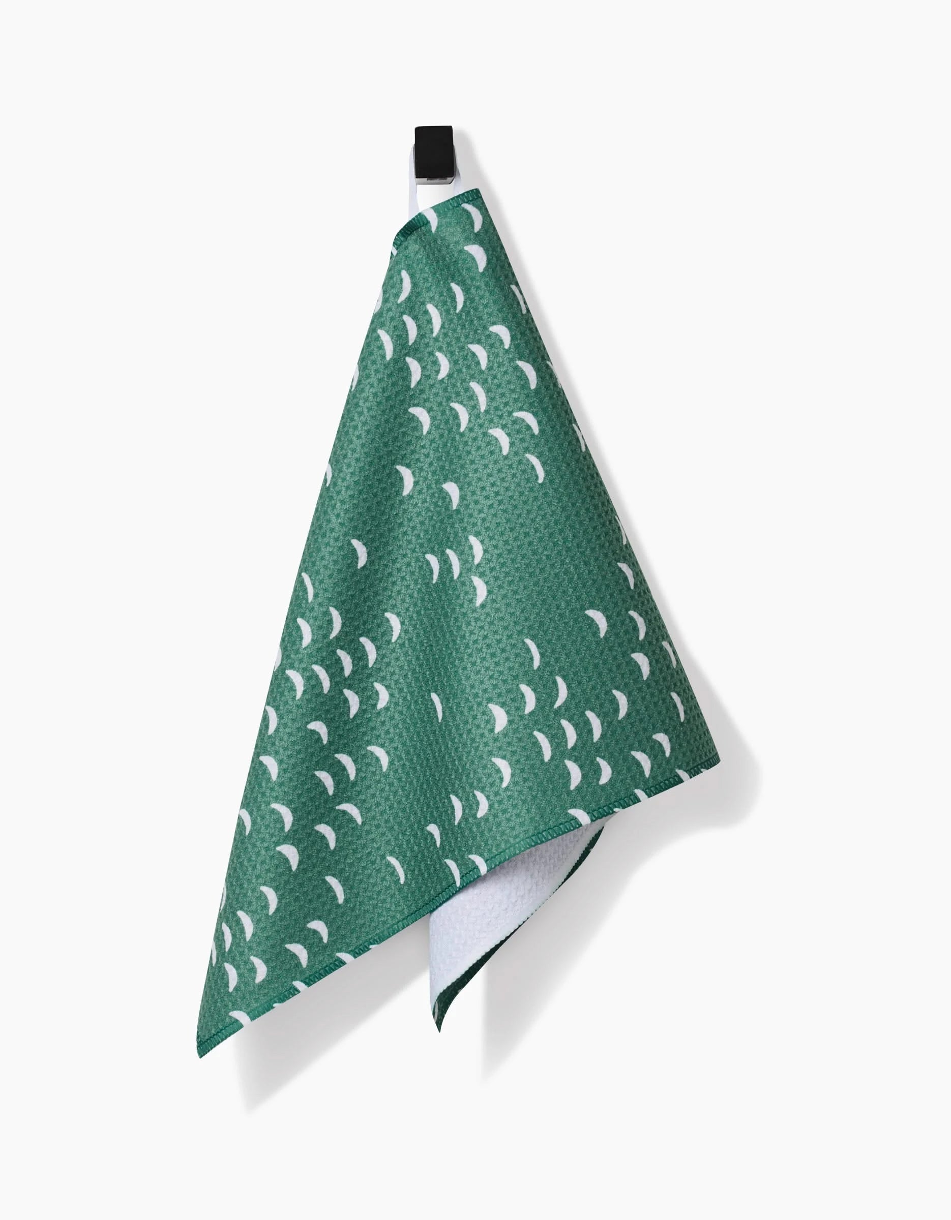 The Jessica Swift Breezeway Bar Towel, made from Geoweave fabric with a green base and small white crescent shapes, hangs by a black loop against a plain white background.