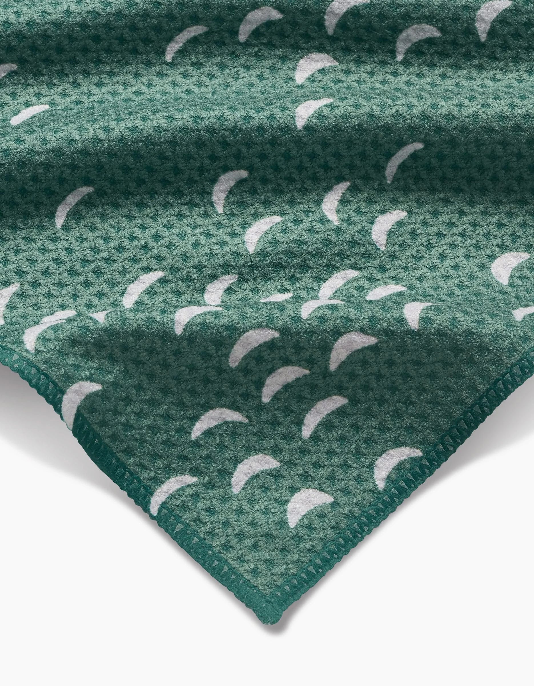 A close-up of the Jessica Swift Breezeway bar towel shows its green Geoweave fabric, white crescent patterns, and neatly stitched edge.